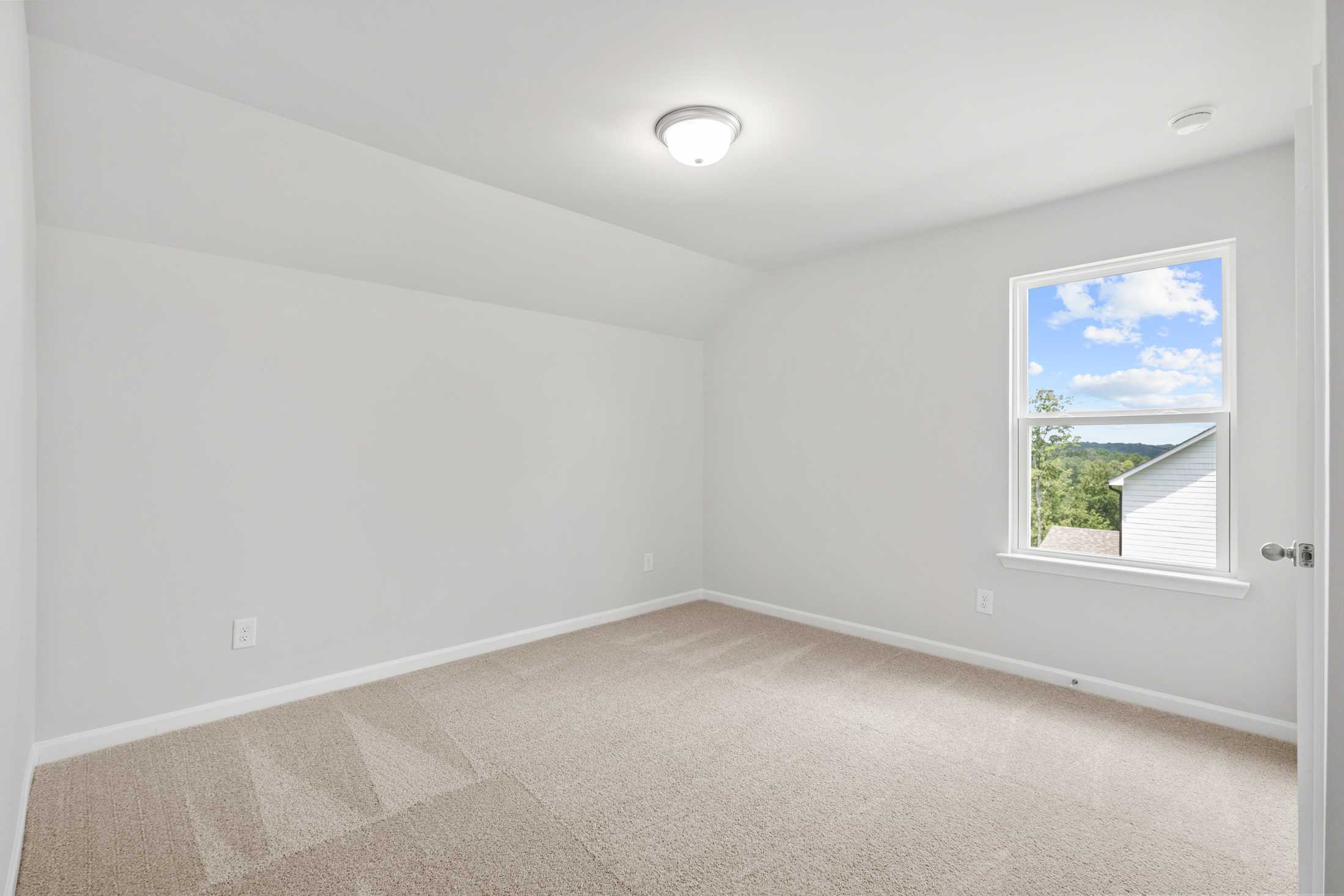 Spacious empty bedroom in The Ash B at Wehunt Meadows with beige carpet, white walls, large window overlooking Georgia greenery