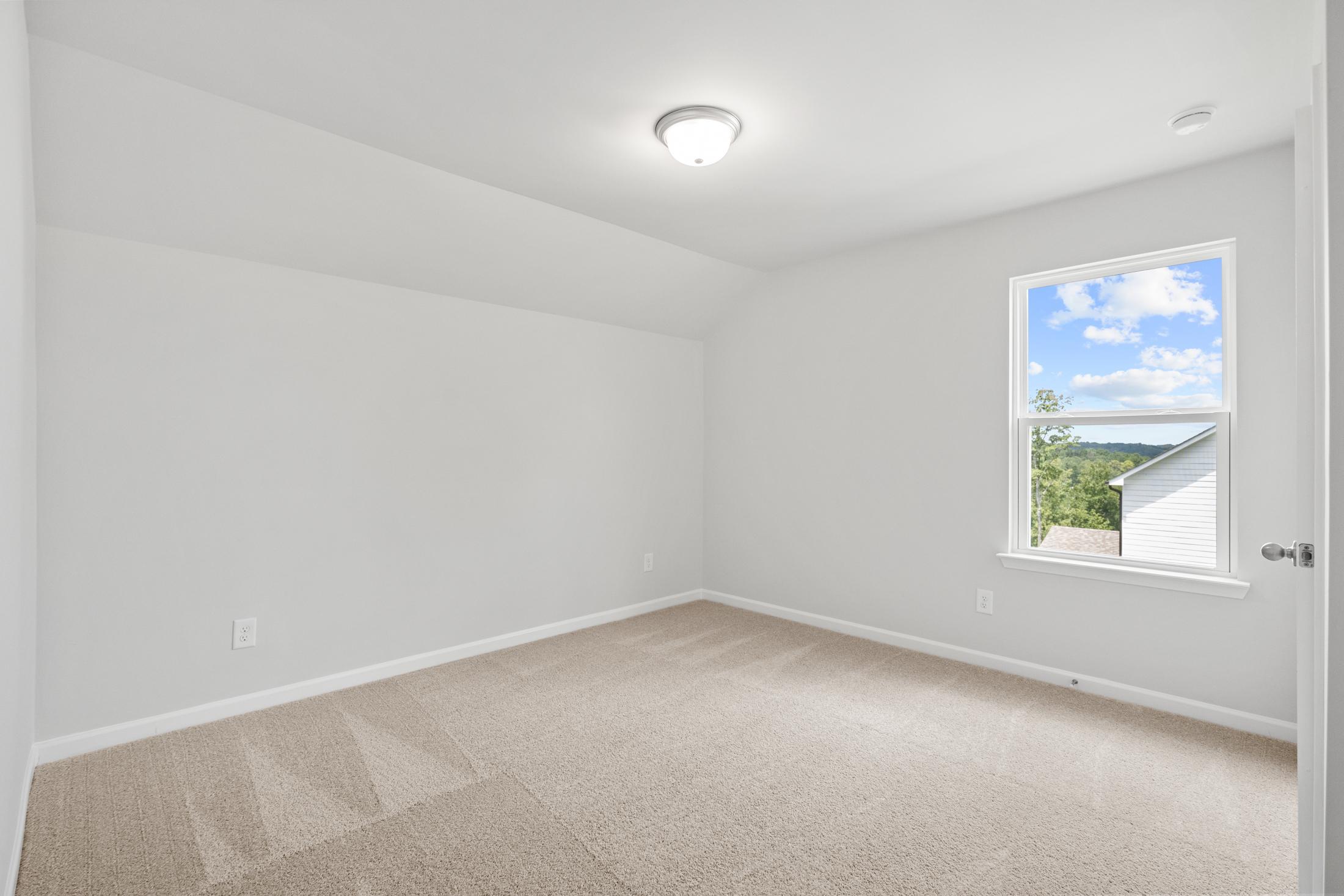 Spacious empty bedroom in The Ash B at Wehunt Meadows with beige carpet, white walls, large window overlooking Georgia greenery
