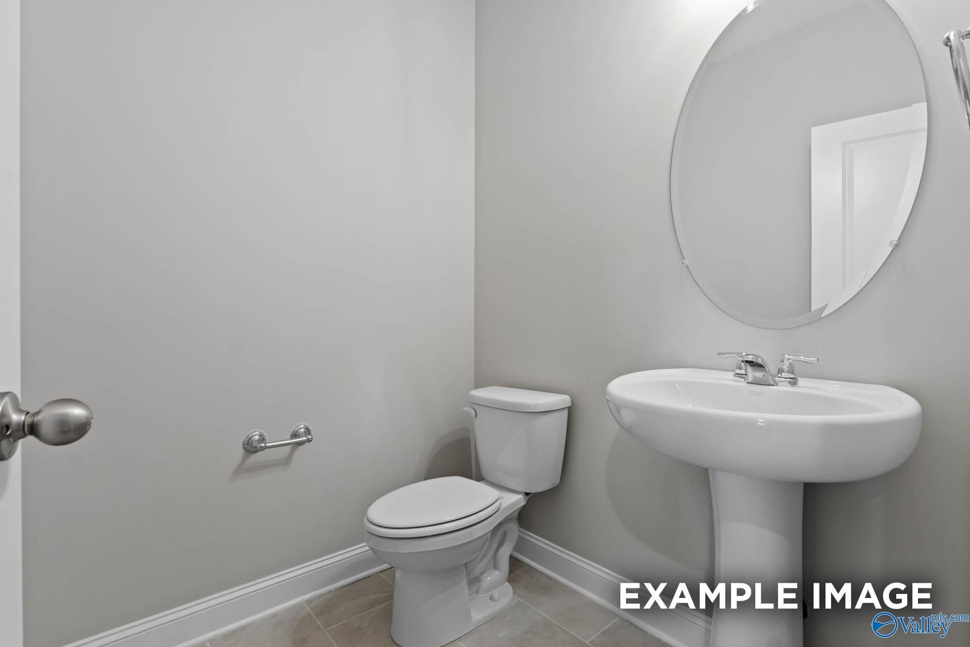 Elegant half bath with round mirror, pedestal sink, and toilet in Davidson Homes The Finleigh, Creekside, Harvest, Alabama