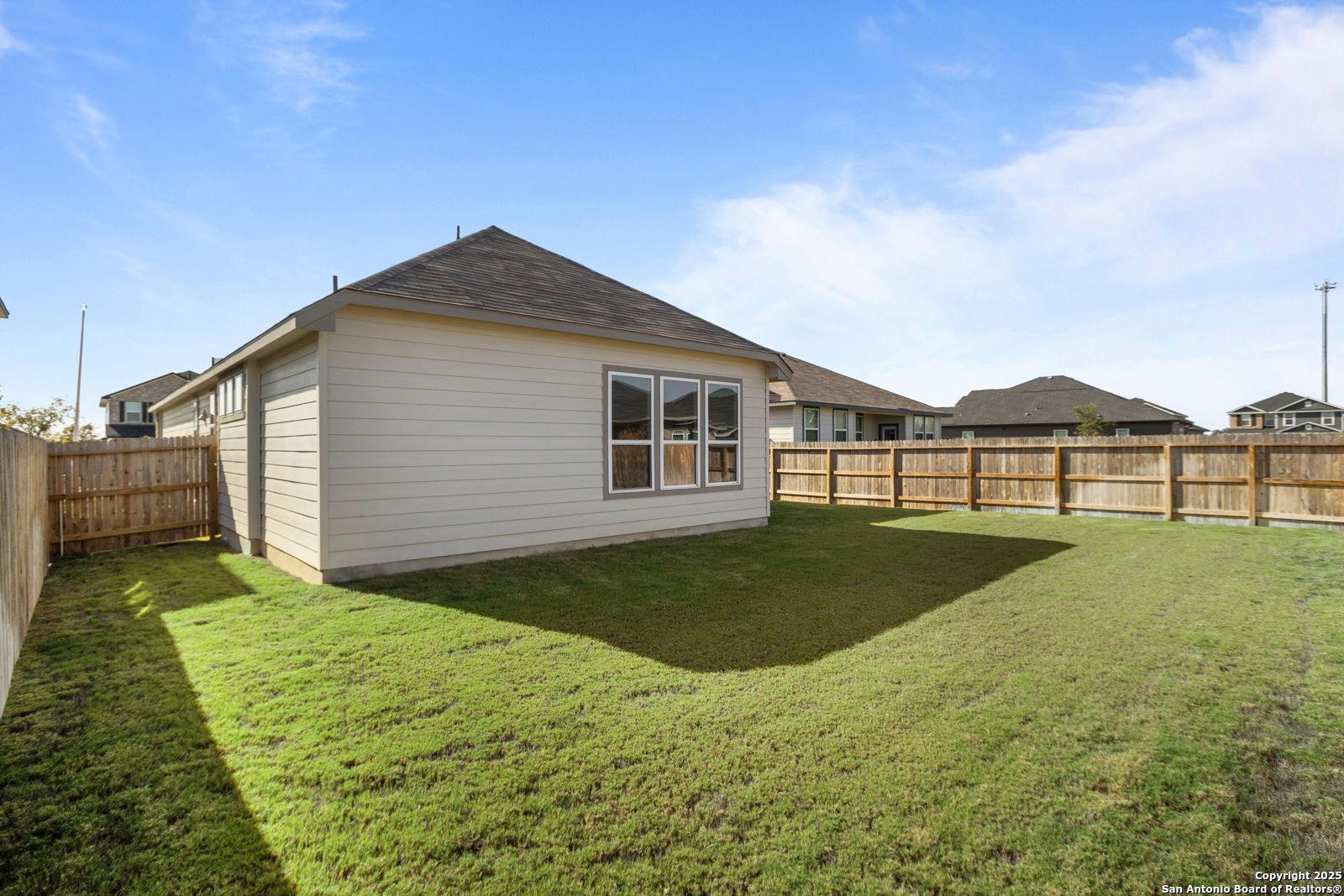 Side view of The Collin B single-story home with beige siding, large windows, and fenced grassy backyard in Hannah Heights, Seguin, Texas