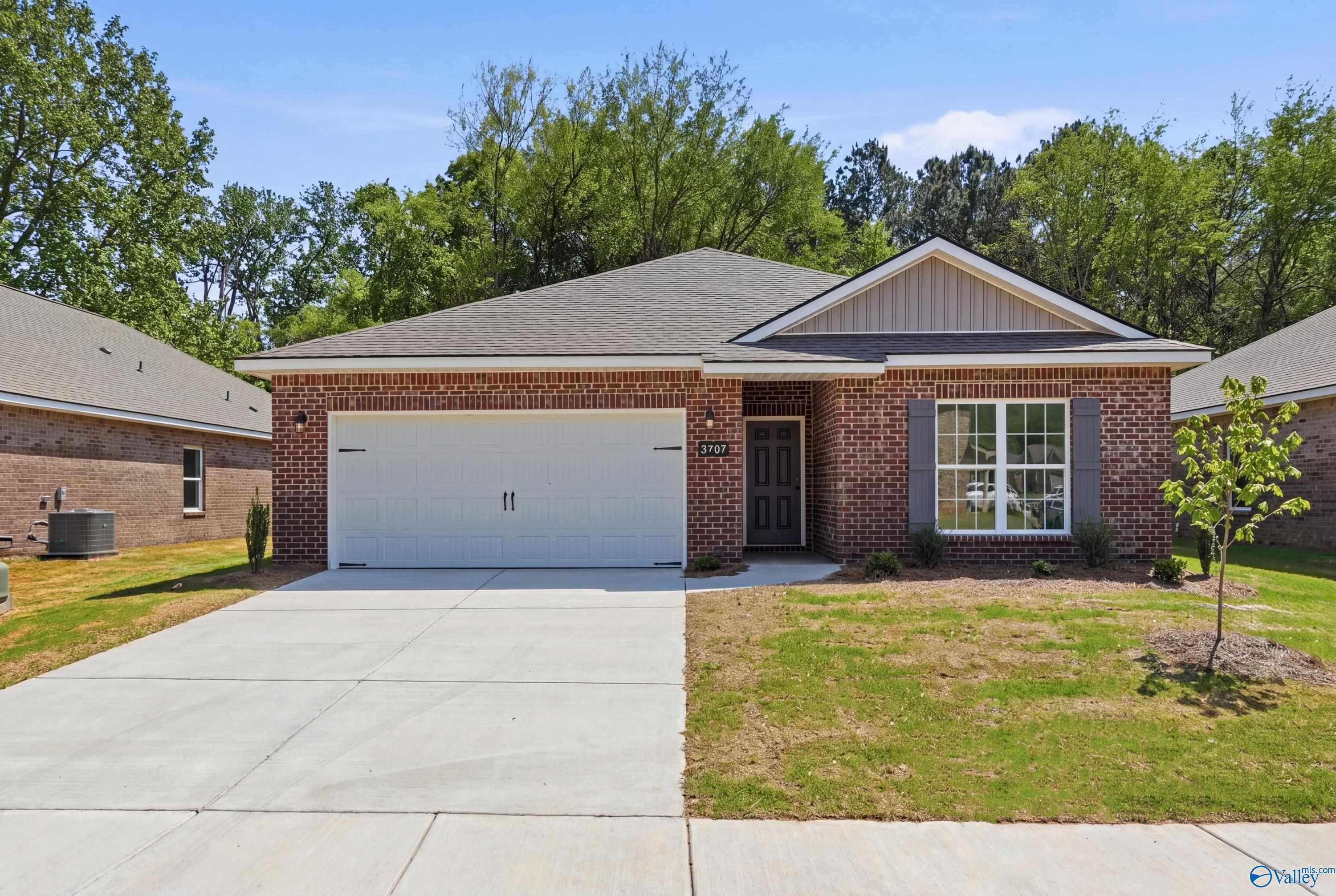 Brick single-story home with 2-car garage, red brick facade, large front window, driveway, and lush lawn in Jaguar Hills, Huntsville, Alabama