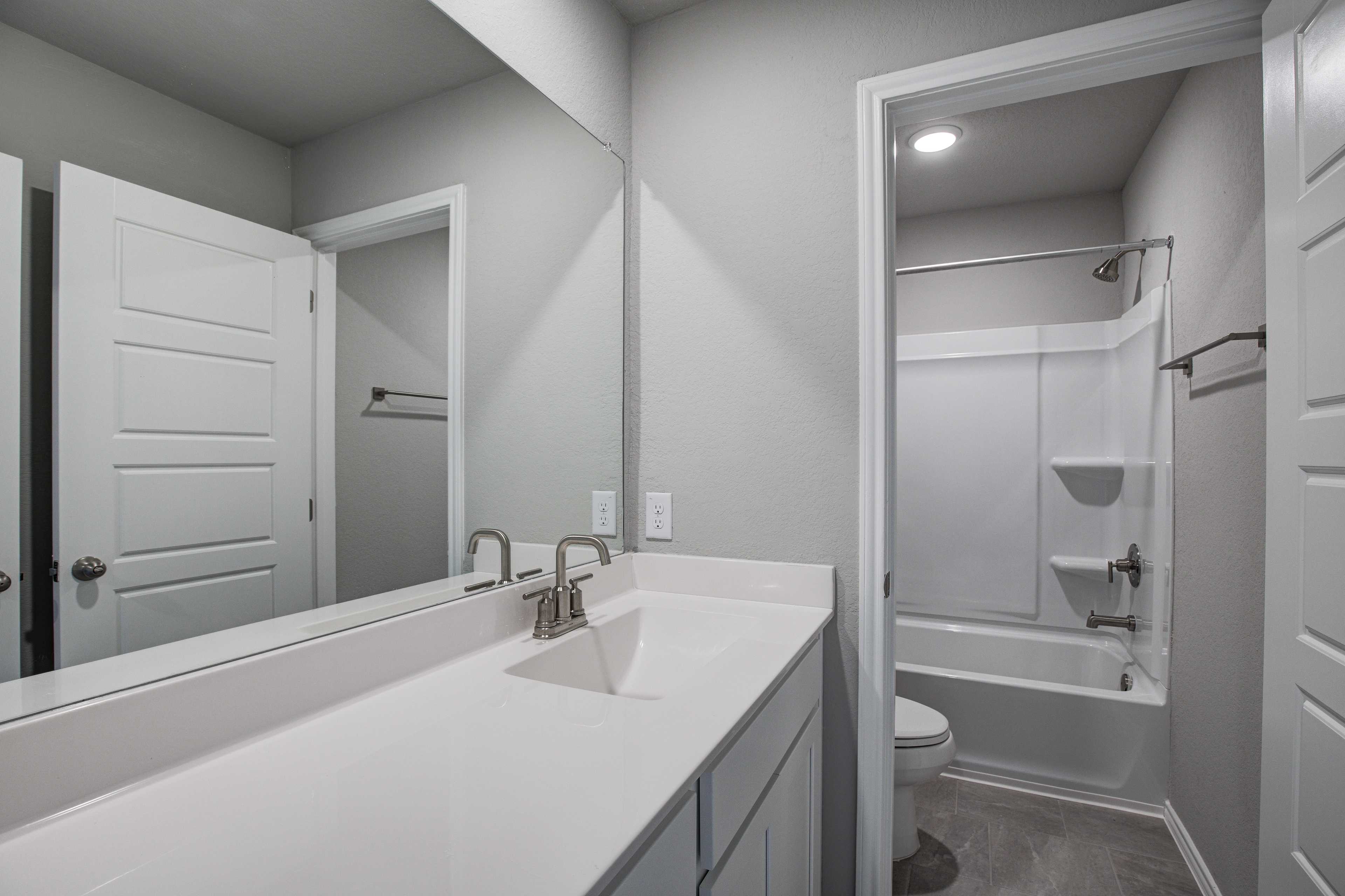 Spacious bathroom in The Blanco B with white vanity, chrome faucet, large mirror, tub-shower combo, and neutral gray tones