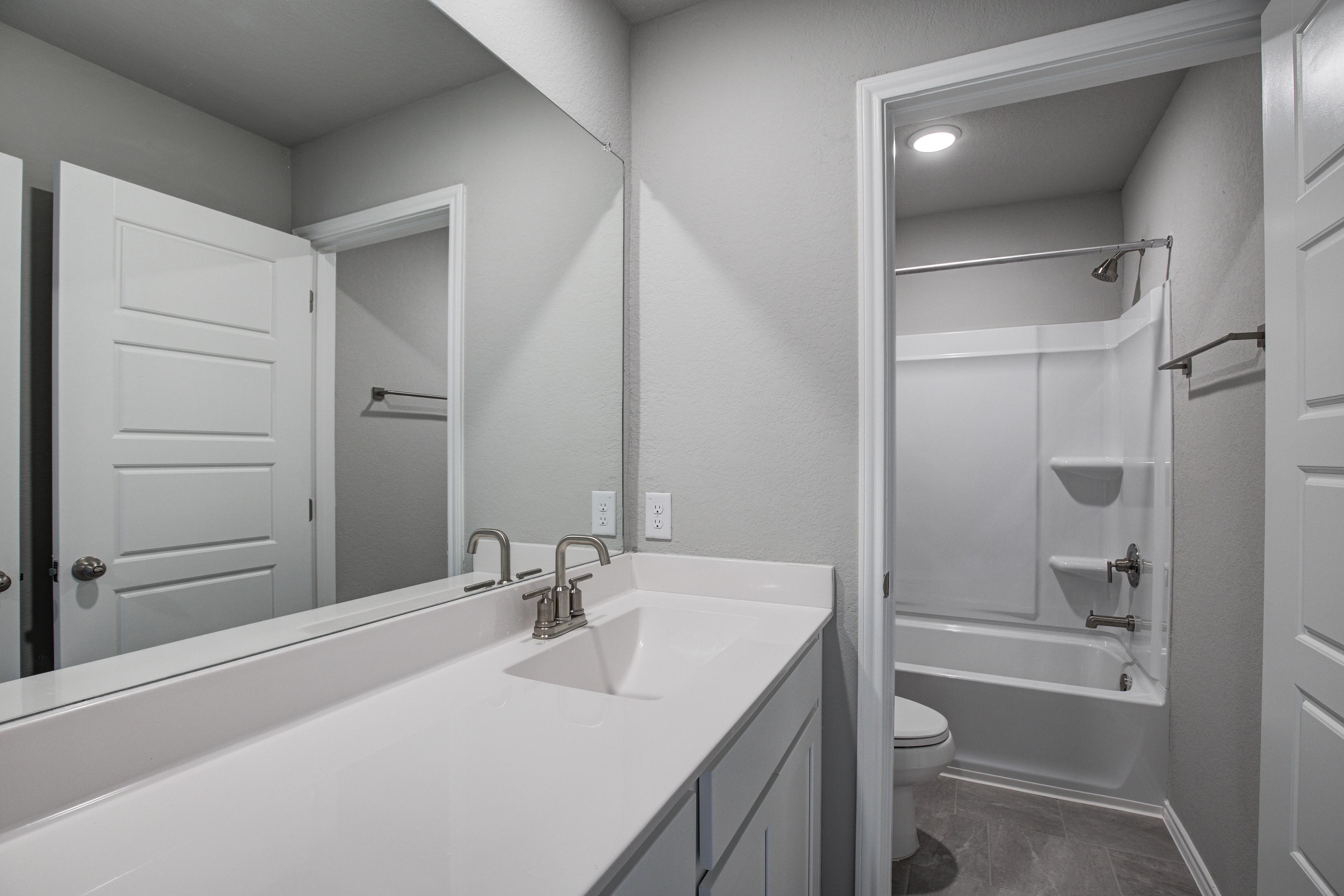 Guest bathroom in The Blanco C home by Davidson Homes, San Antonio, with white vanity, large mirror, tub-shower combo