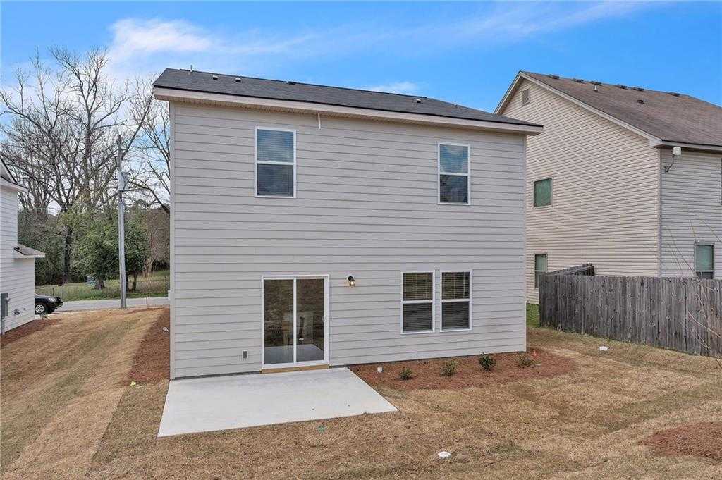 Rear view of The Bartlett 2-story home with sliding glass doors to concrete patio, fenced backyard, and shrubs in Summer Vineyard, Phenix City, Alabama