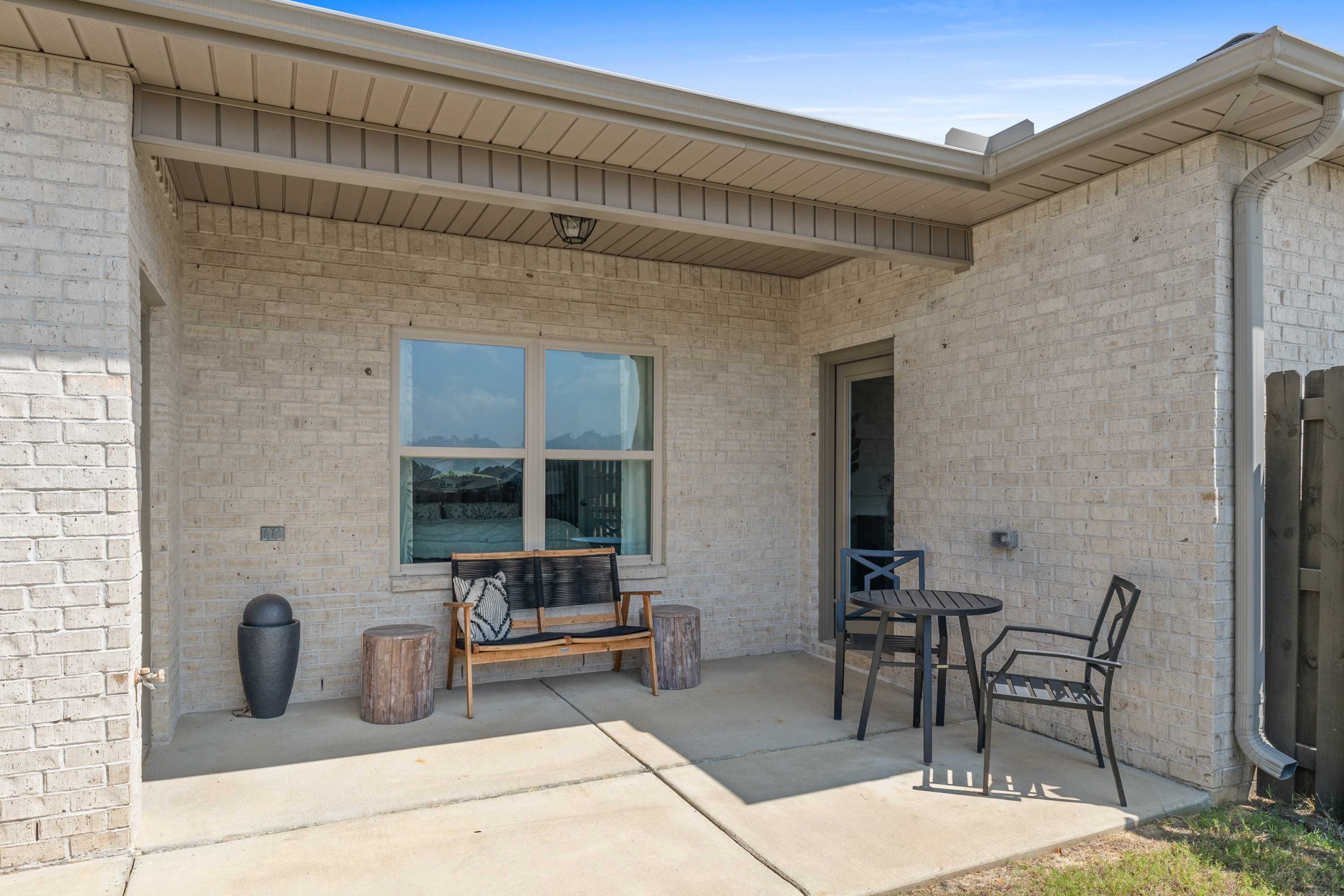 Covered patio with beige brick walls, cushioned bench, bistro set and potted plant at The Retreat at Cain Park in Hartselle AL