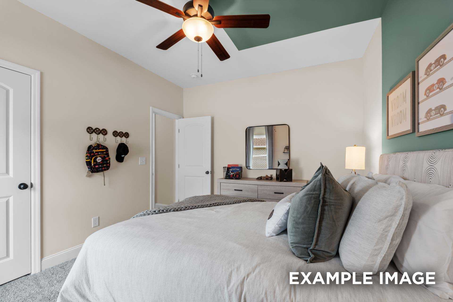 Cozy master bedroom in The Laurel N with king bed, green pillows, ceiling fan, beige walls, and nightstand lamp