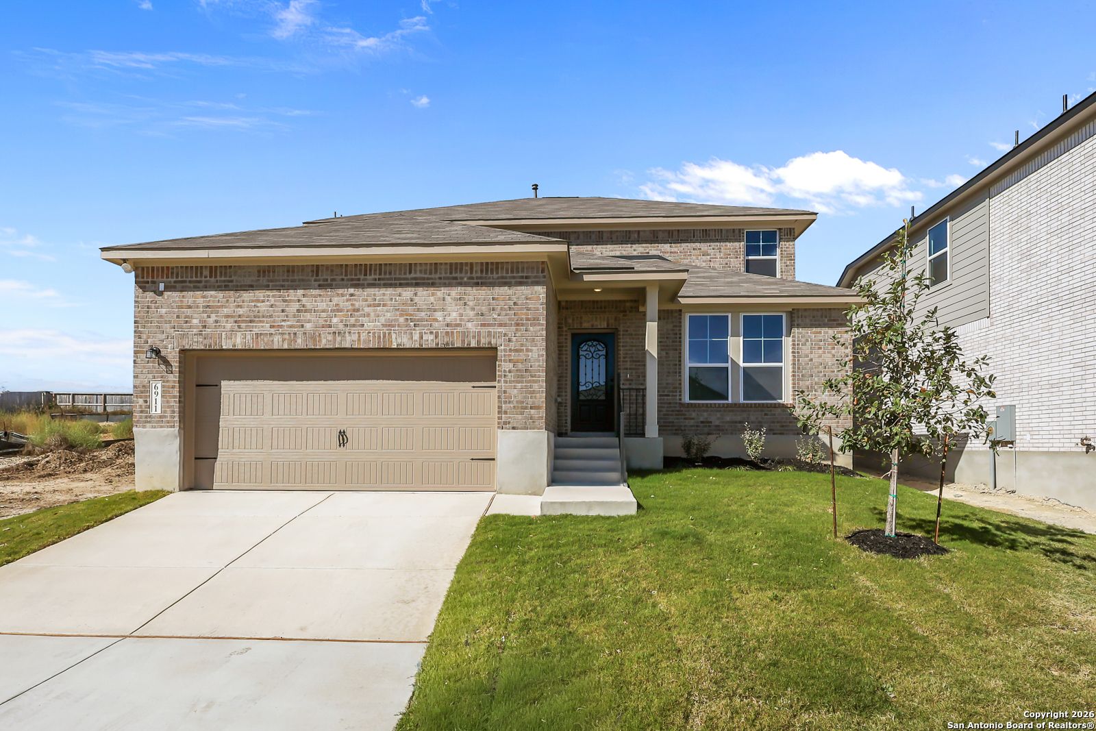 Modern brick facade of 4-bedroom Davidson Homes The Douglas E in Comanche Ridge, San Antonio, Texas, with 2-car garage and lush front lawn