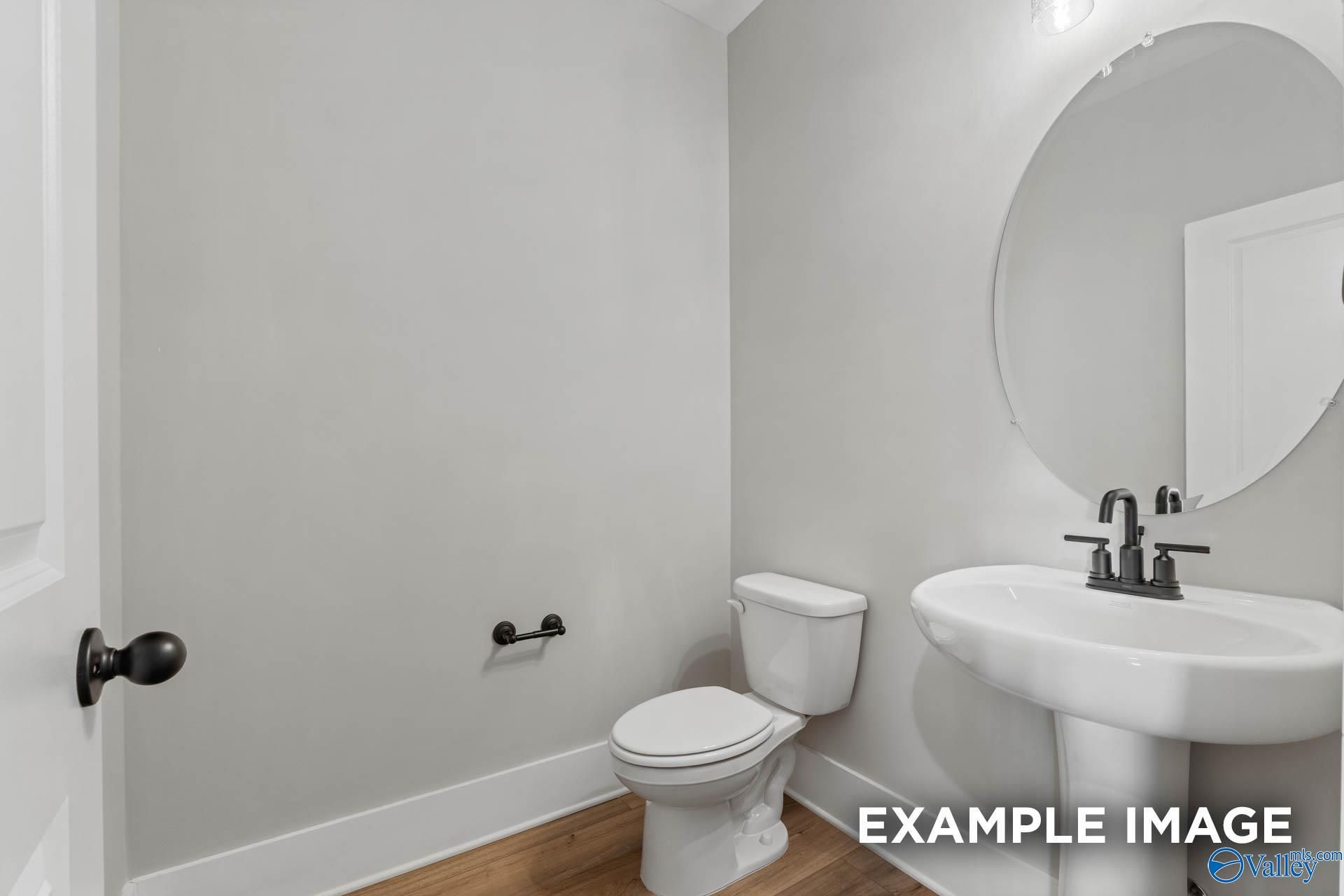 Modern powder room with pedestal sink, round mirror, and wood-style flooring in The Finleigh home at Briercreek, Alabama.