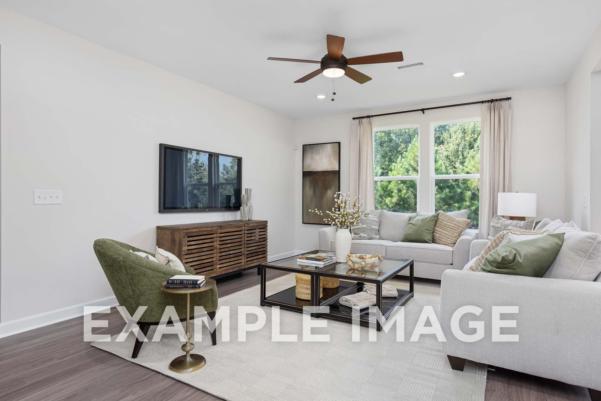 Spacious living room in The Willow E by Davidson Homes, Angier NC, featuring L-shaped sofa, wall-mounted TV, and large window views