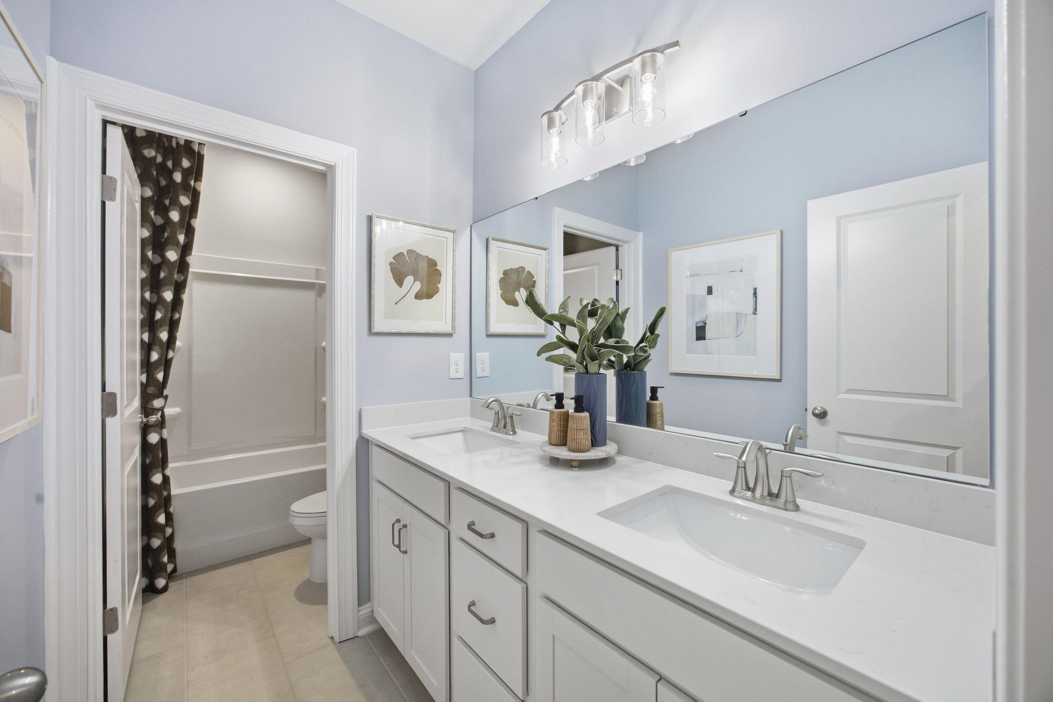 Spacious modern bathroom at Enclave at Belmont in Belmont NC with light blue walls, double quartz vanity, bathtub
