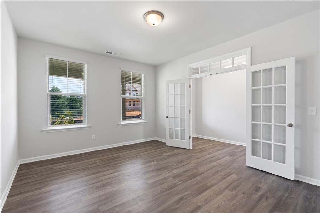 Bright formal living room with hardwood floors, open French doors, and window views in Davidson Homes The Hickory A, Winder, GA