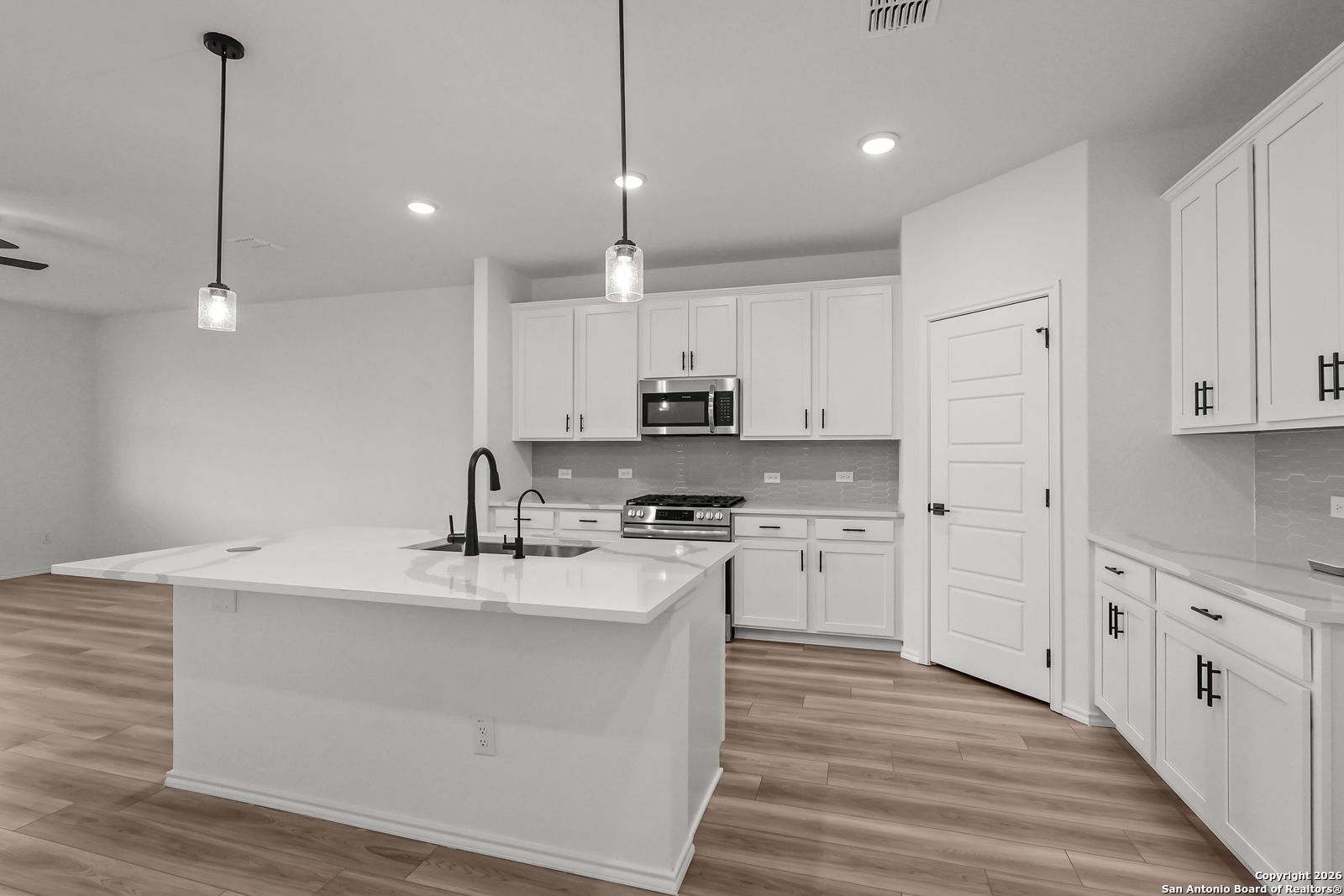 Modern white kitchen with large island sink, stainless appliances, and hardwood floors in Davidson Homes The Douglas E, San Antonio