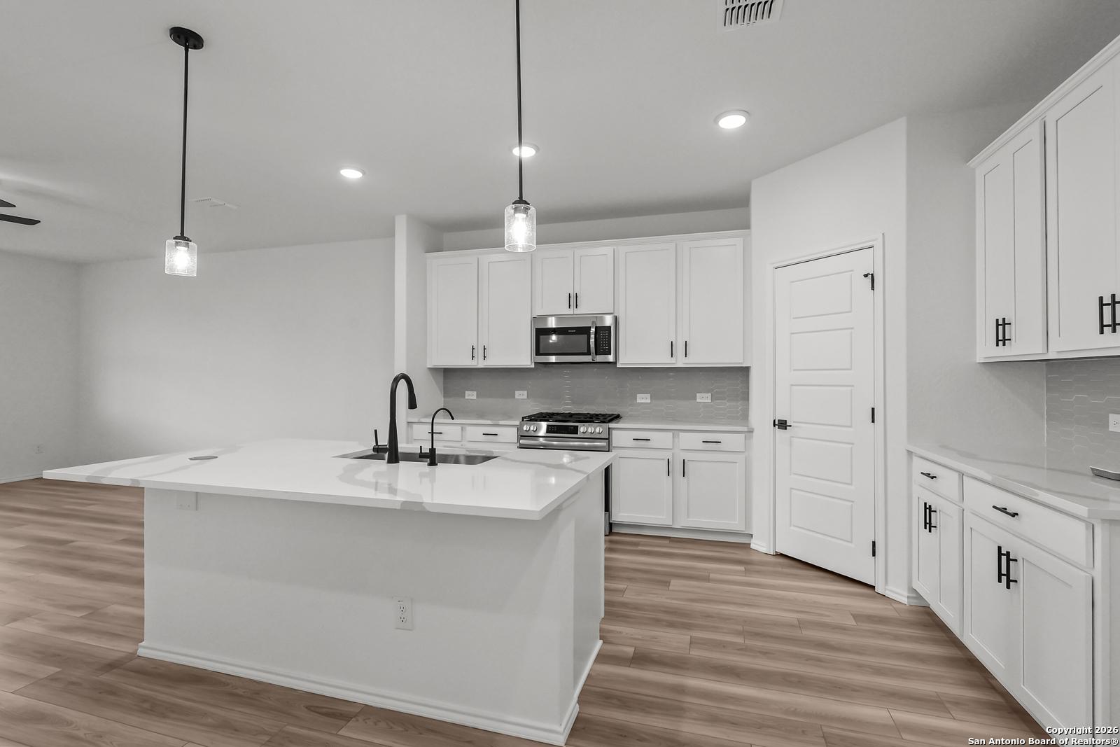Modern white kitchen with large island sink, stainless appliances, and hardwood floors in Davidson Homes The Douglas E, San Antonio