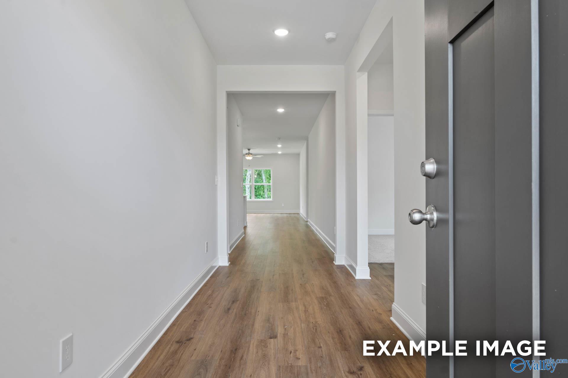 Bright hallway with light oak floors, white walls, and recessed lights in Evermore Homes Daphne E, Harvest, Alabama