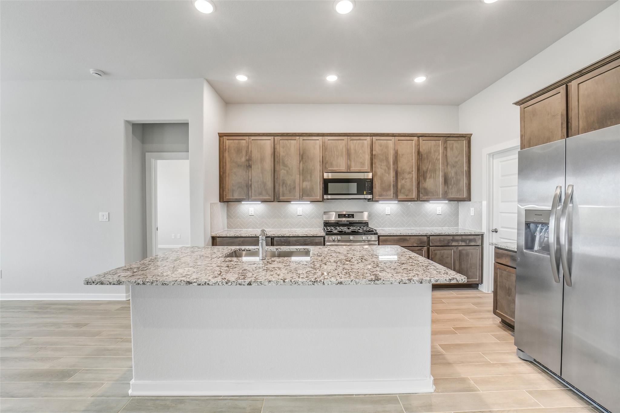 Modern kitchen with granite island, shaker cabinets, stainless appliances in Davidson Homes The Acadia C, Magnolia Texas