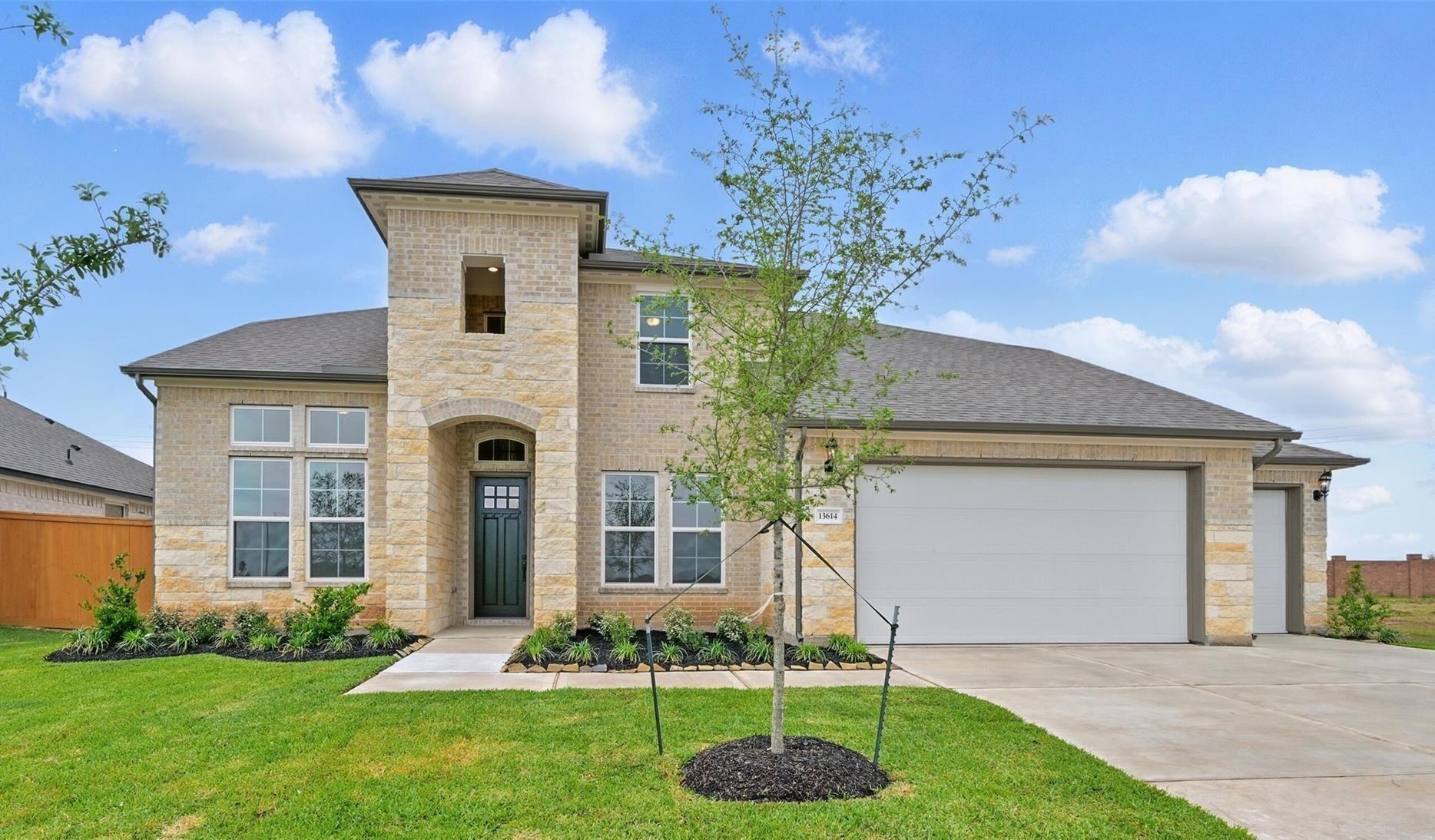 Two-story stone and brick home with arched green door, 4-car garage, young trees, and lush landscaping in Lago Mar, Texas City, Texas