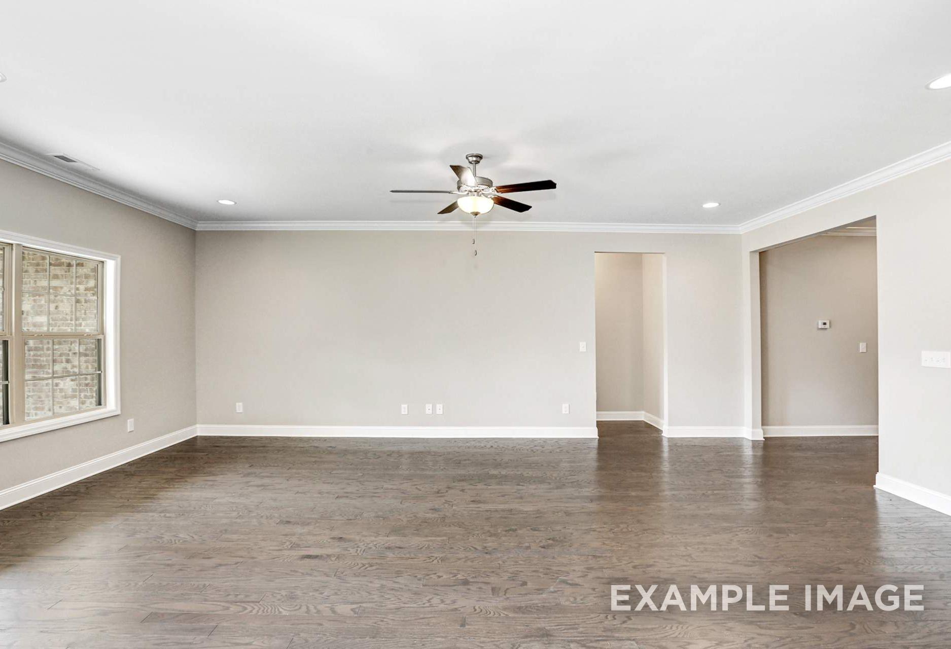 Spacious open-concept living room in The Montgomery home with hardwood floors, ceiling fan, and large beige-shuttered windows