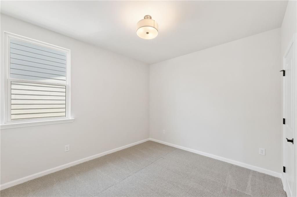 Bright secondary bedroom featuring white walls, large window with blinds, and plush carpet in Davidson Homes The Daphne C, Loganville, GA