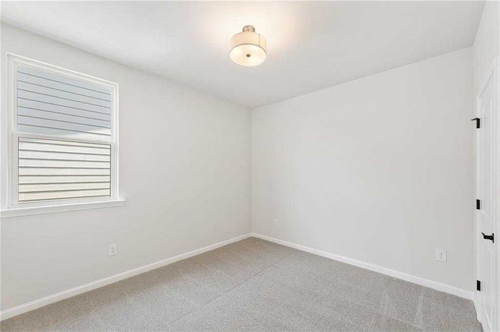Bright empty bedroom with white walls, large window blinds, carpet floor, and ceiling light in Davidson Homes The Daphne C, Loganville, GA