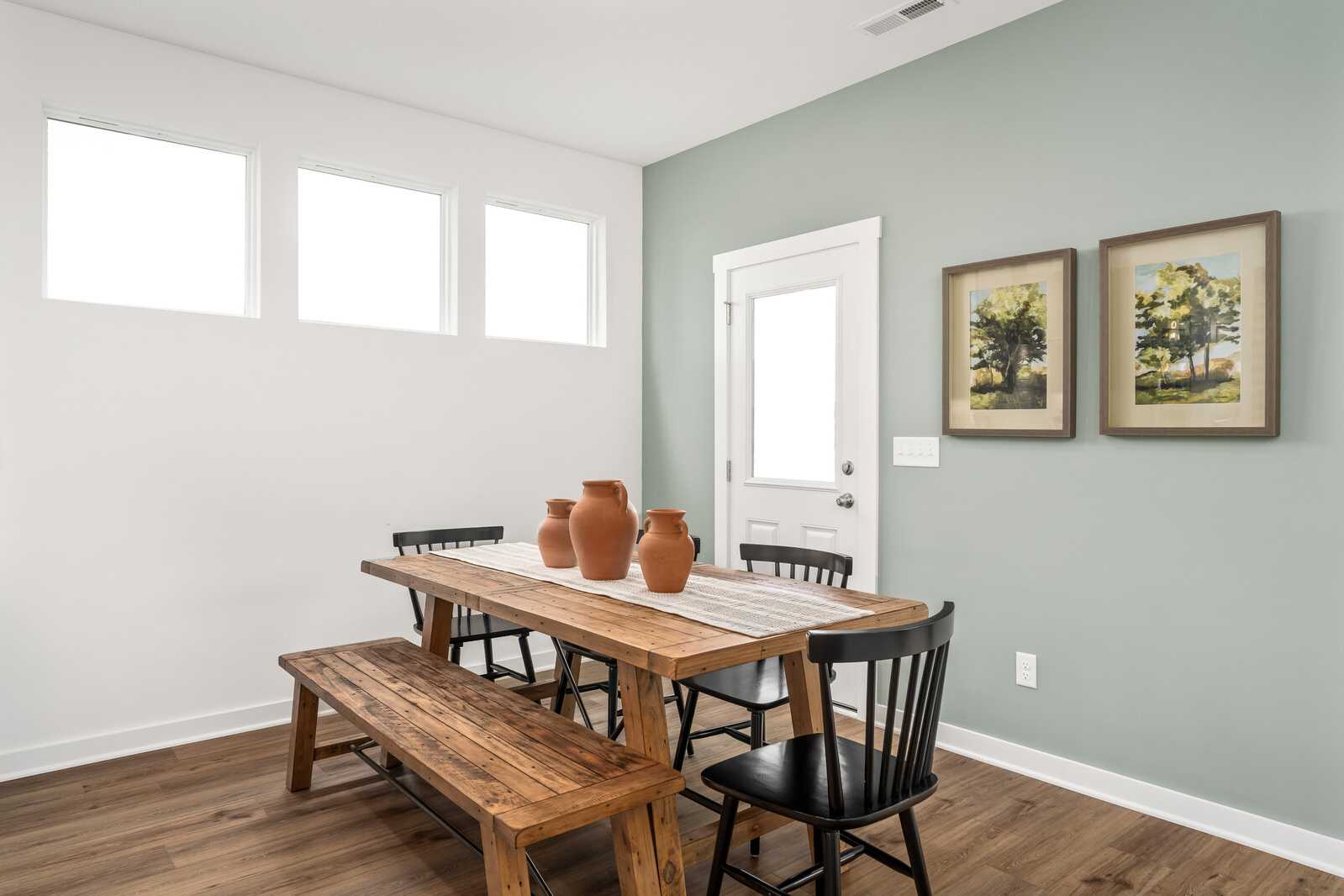 Rustic dining room at Calista Farms in White House, Tennessee with wooden table, benches, black chairs, terracotta vases, hardwood floors, and large windows