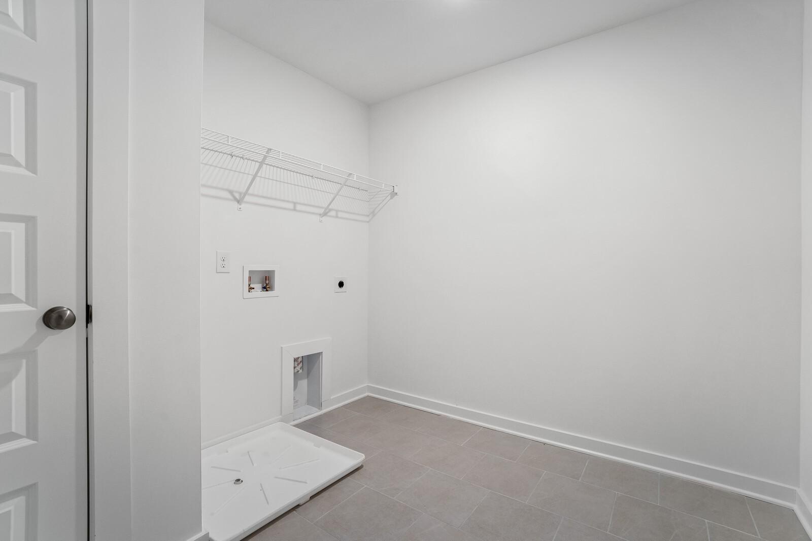 Bright white laundry room with utility sink, wire shelving, and tiled flooring in Davidson Homes The Logan C, Calista Farms, White House, TN