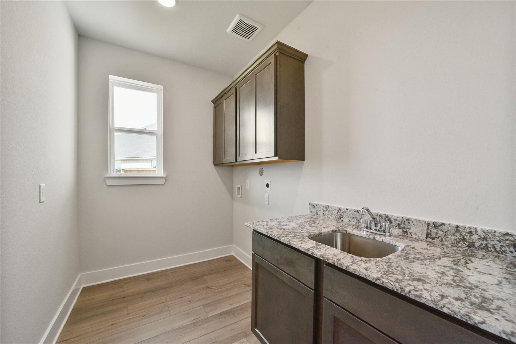 Modern laundry room featuring quartz countertop, shaker cabinets, sink, and hardwood floors in Davidson Homes The Zion A, Texas City, Texas