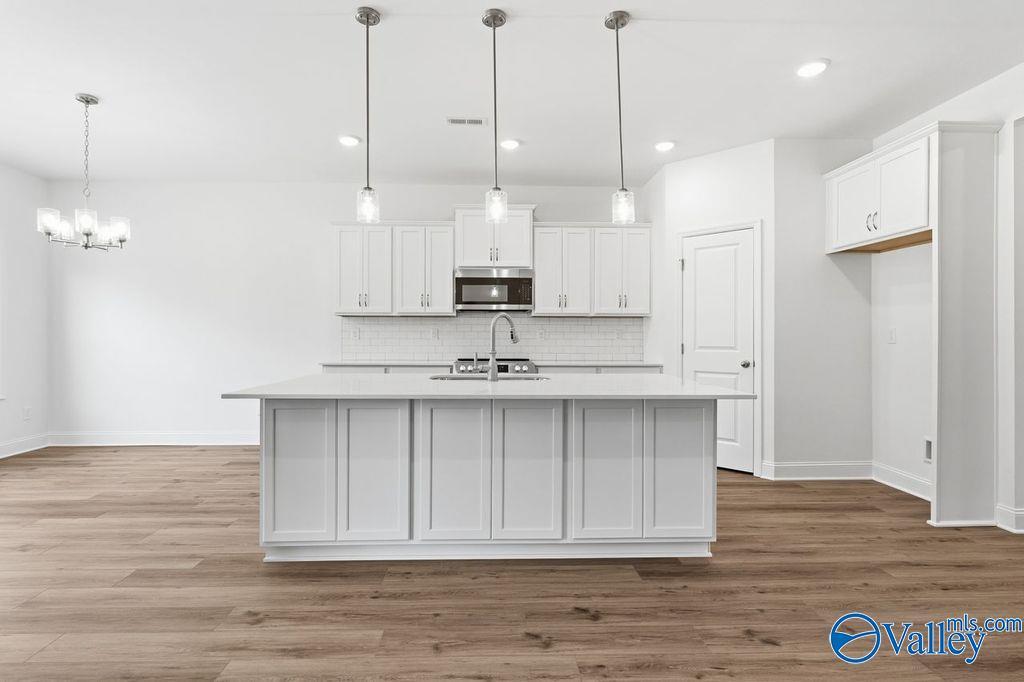 Modern white kitchen with large island sink, stainless appliances, pendant lights in The Montgomery floor plan, Hartselle, Alabama