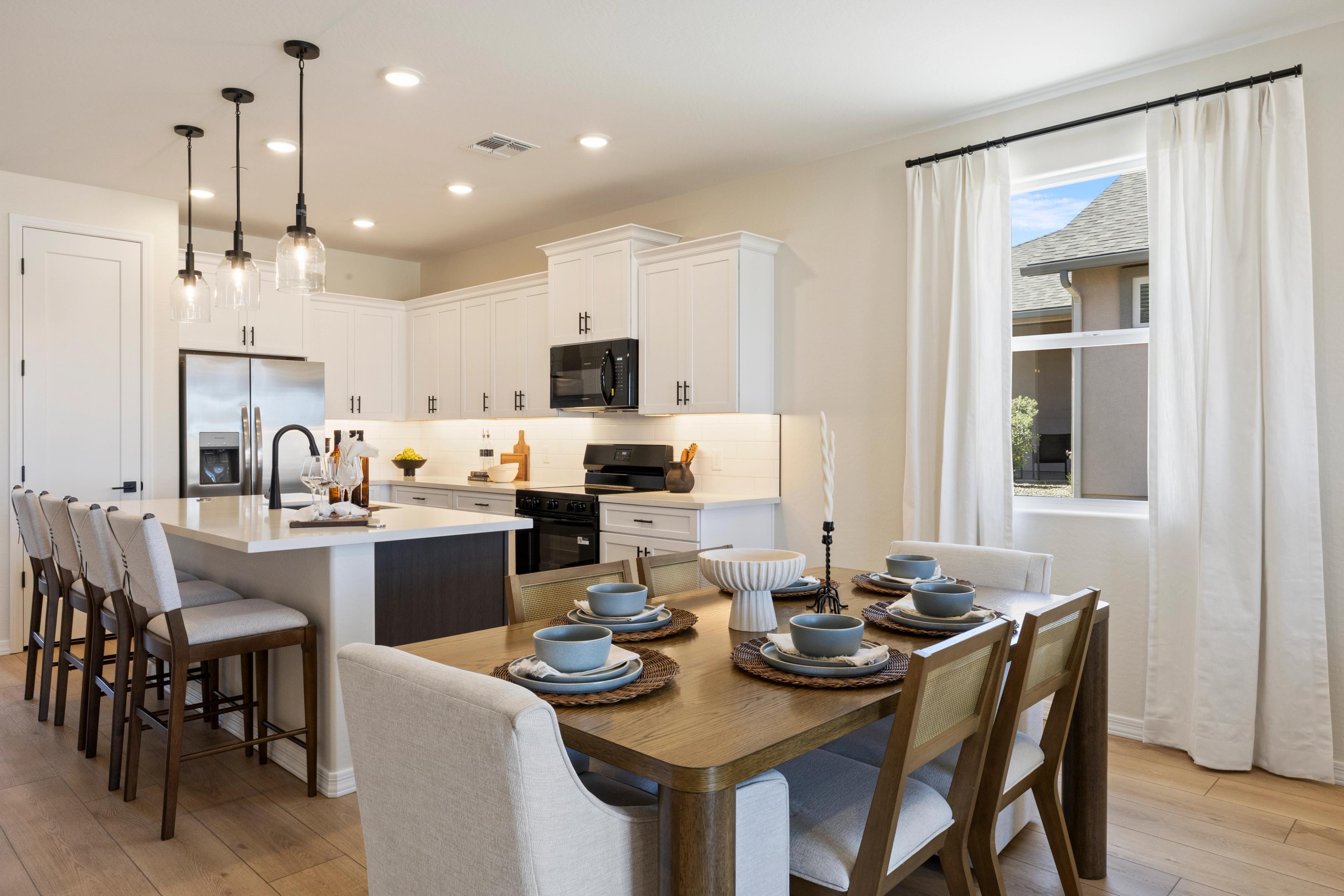 Modern open-concept kitchen with white cabinets, stainless appliances, island bar, and dining nook at Vineyards at Cottonwood in Cottonwood AZ