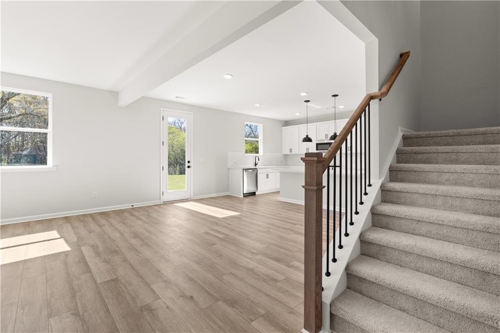 Open living area with hardwood floors, wooden staircase, and adjacent kitchen in The Hickory B by Davidson Homes, Winder, GA