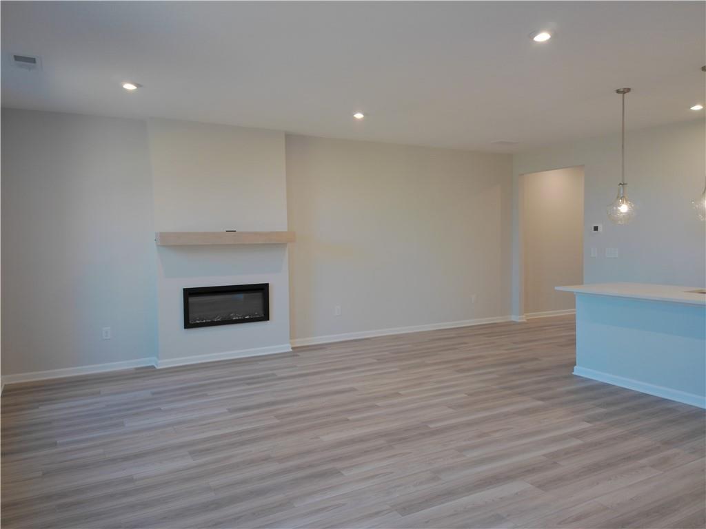Cozy open living room with modern white fireplace, hardwood floors, and pendant lights in Davidson Homes The Marion C, Winder, GA