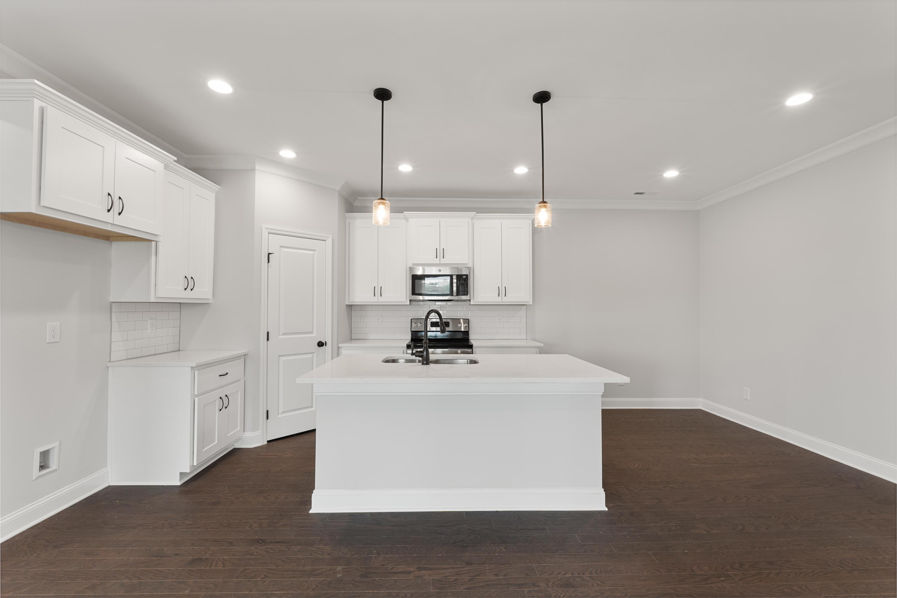 Spacious white kitchen in The Copeland featuring large center island, farmhouse sink, shaker cabinets, and hardwood floors