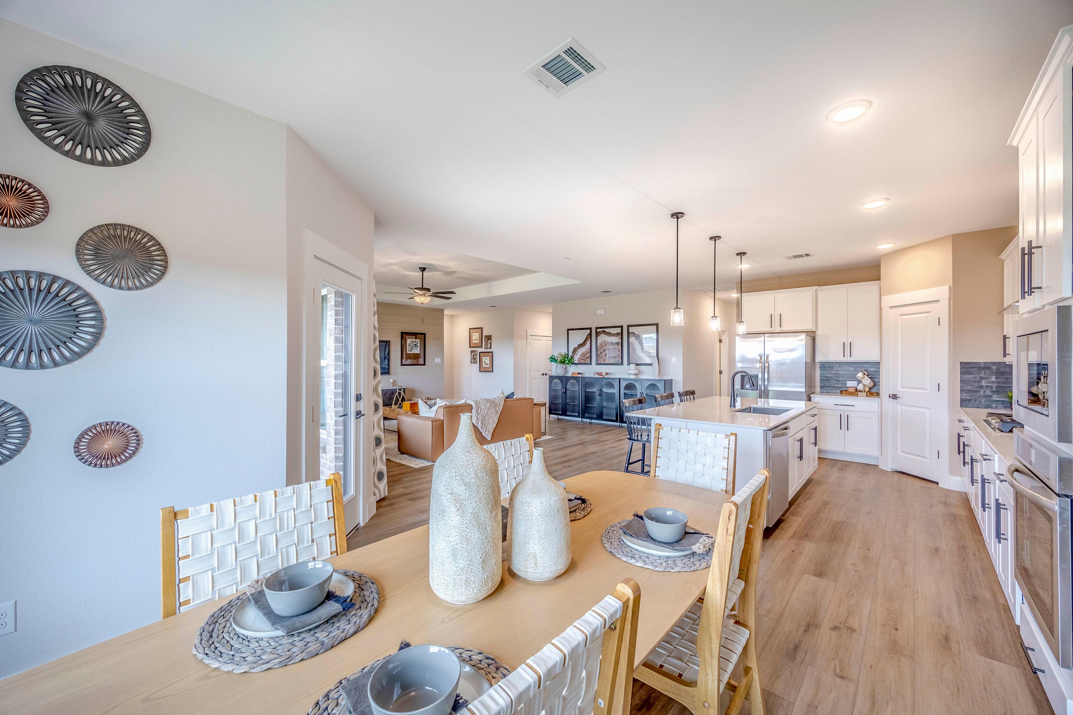 Open-concept dining and kitchen in Waverly Estates home by Davidson Homes in Josephine Texas with wooden table, white cabinets, and hardwood floors
