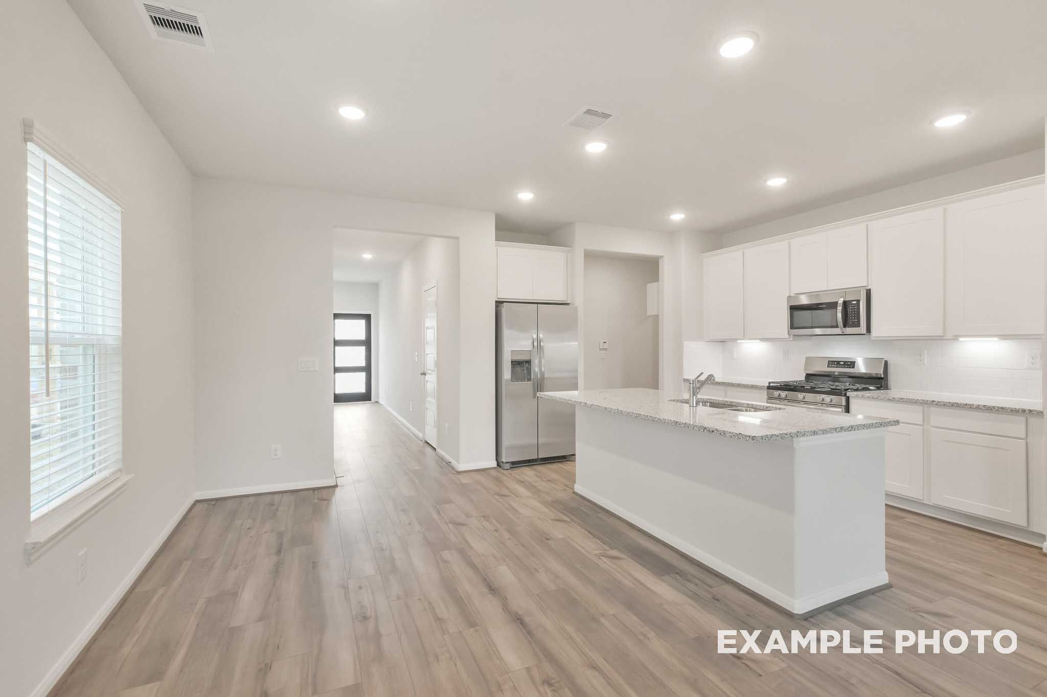 Bright open-concept kitchen in The Brazos by Davidson Homes, featuring white cabinetry, granite island, and stainless appliances.