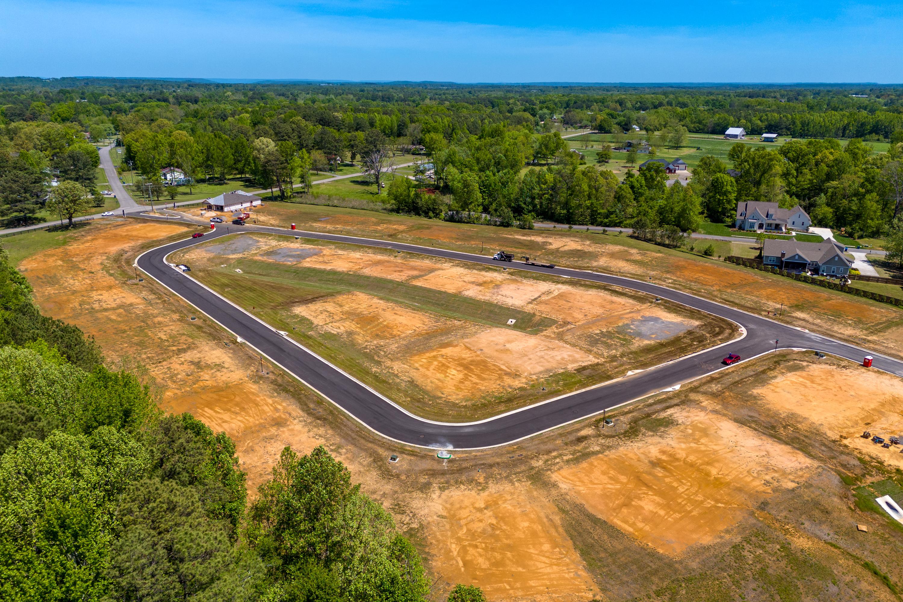 Aerial view of curved asphalt roads and home sites under construction at The Highlands in Arab, Alabama by Davidson Homes amid lush forests