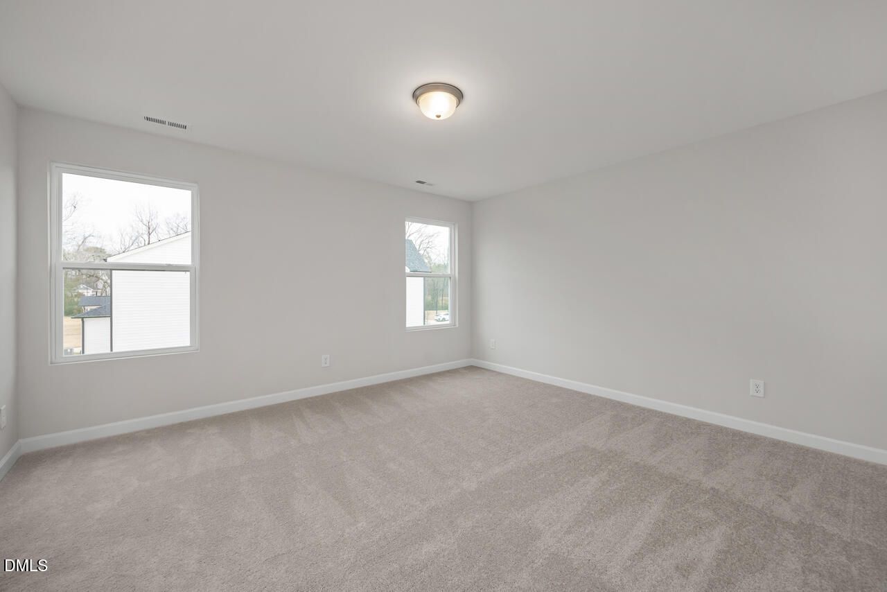 Empty secondary bedroom featuring light gray walls, beige carpet, and large windows in Davidson Homes The Gavin B, Lillington, NC