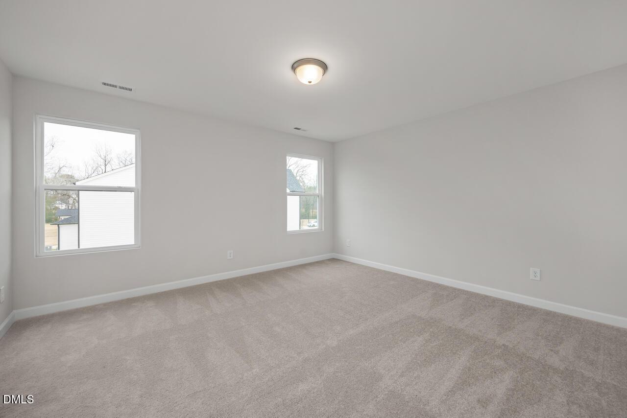 Empty secondary bedroom featuring light gray walls, beige carpet, and large windows in Davidson Homes The Gavin B, Lillington, NC
