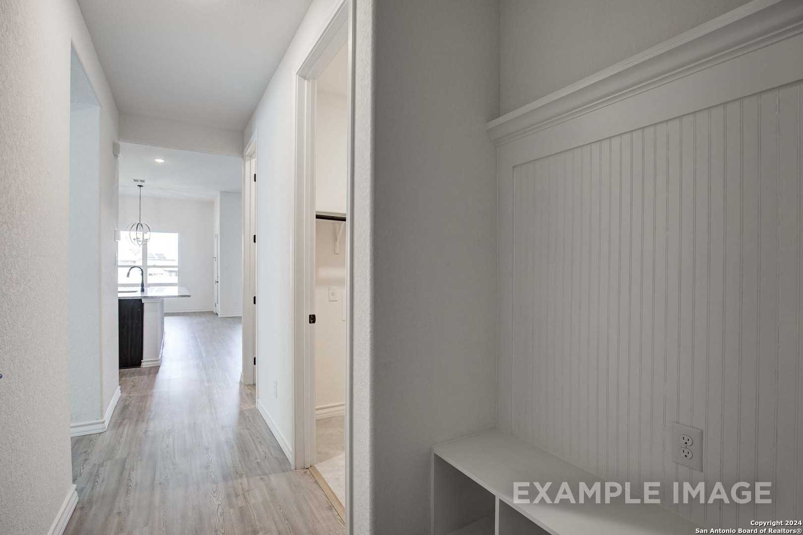 Spacious entry hallway with shiplap bench, coat hooks, and wood floors leading to kitchen in 4-bedroom Davidson Homes The Garner C, Castroville, Texas