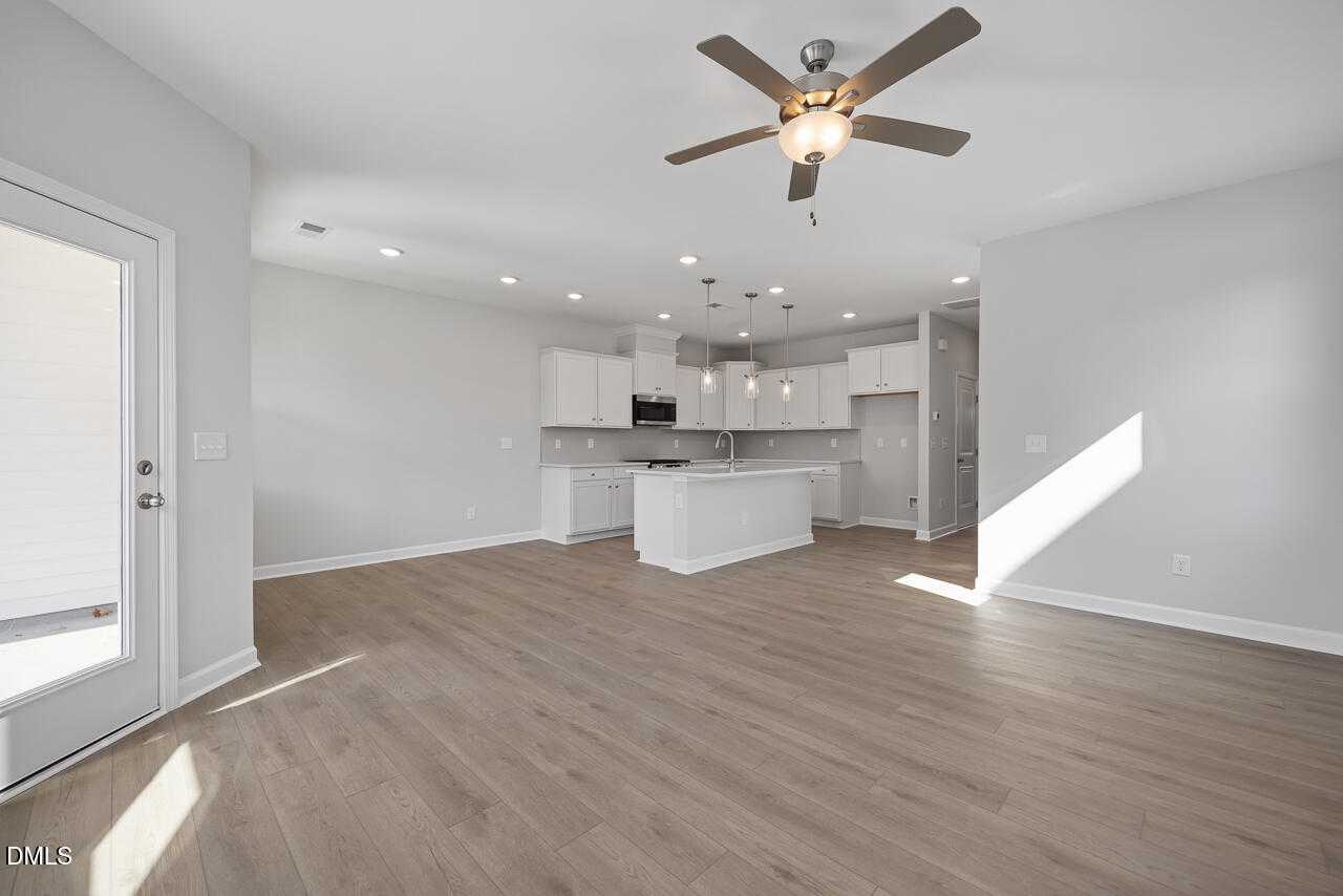 Open-concept kitchen with white cabinets, stainless appliances, island, and hardwood floors in The Graham 3-bedroom home, Fuquay-Varina, NC