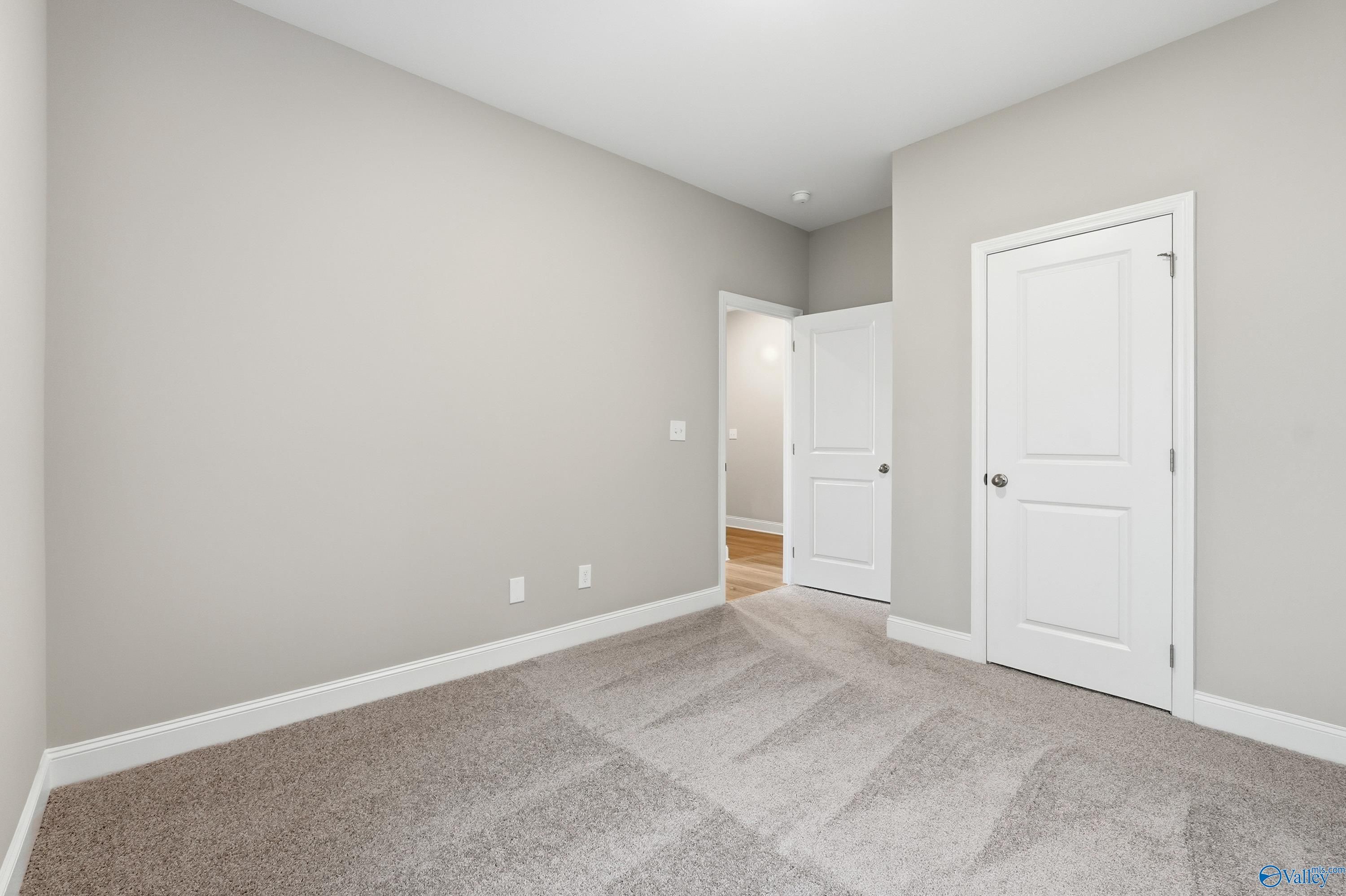 Bright secondary bedroom with light gray walls, beige carpet, and white doors in Davidson Homes The Asheville, Arab, Alabama