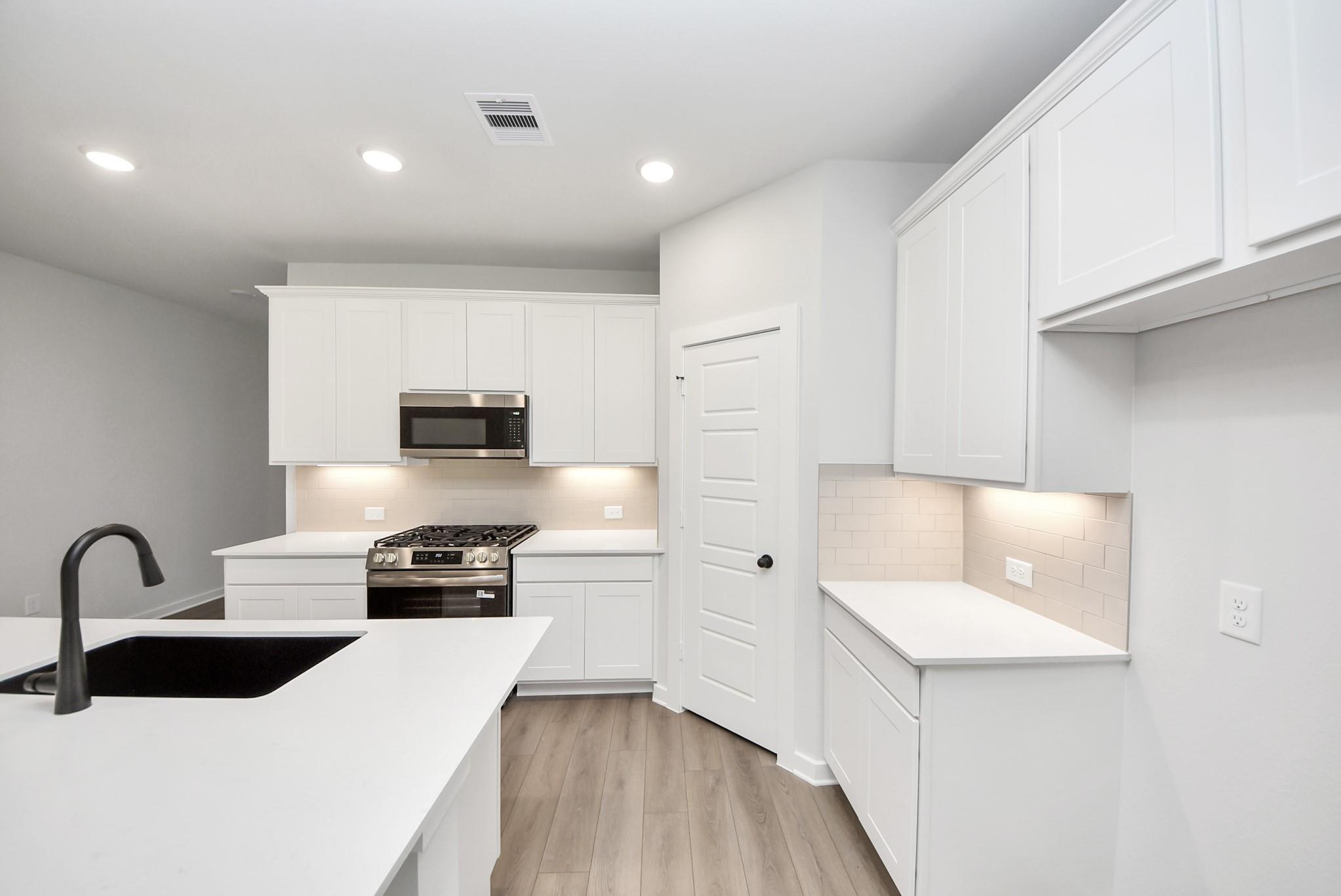 Modern kitchen with white cabinets, stainless steel appliances, and island in The Daphne F floor plan, Crosby, Texas.