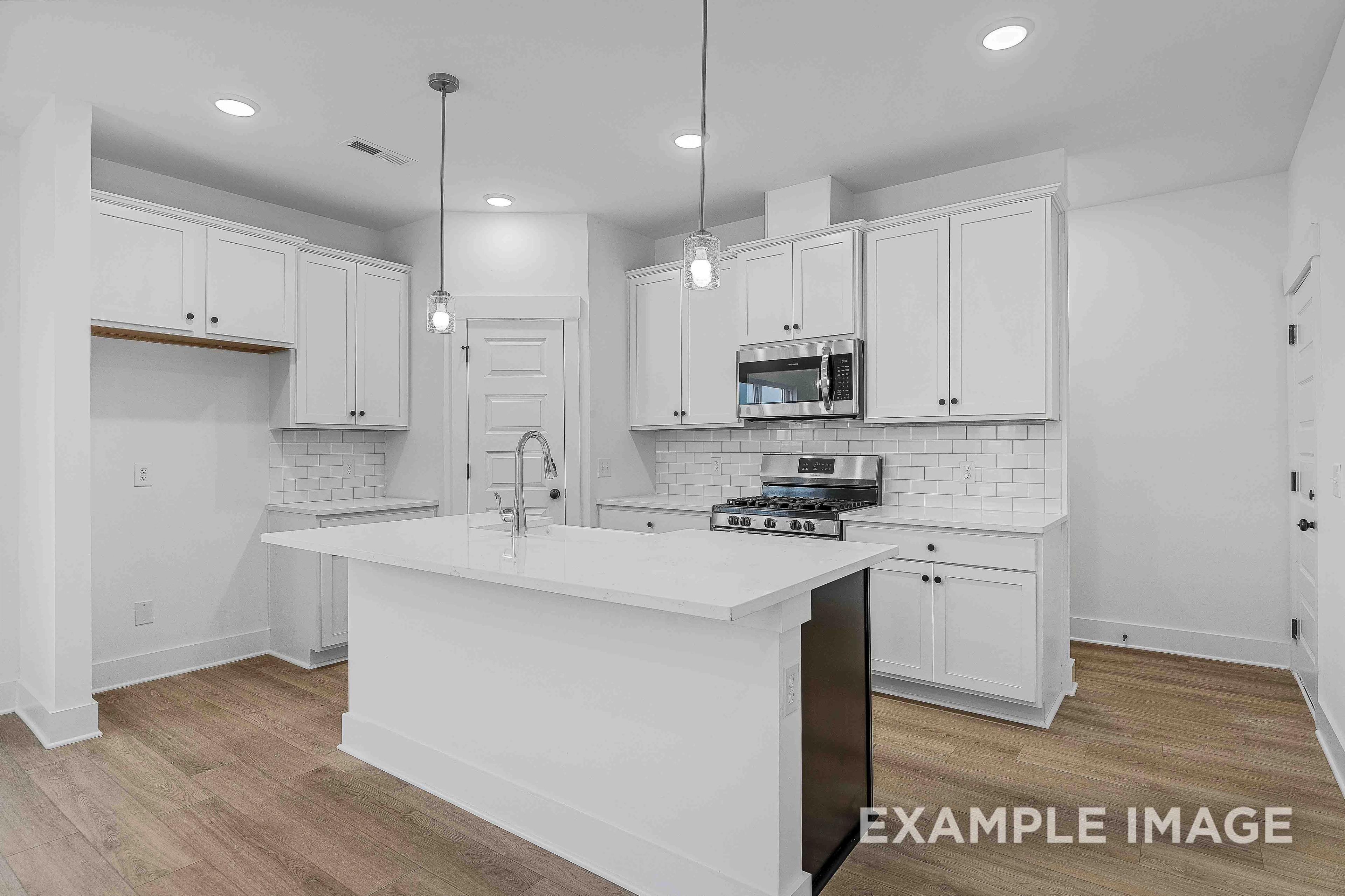 Bright open kitchen in The Charleston home with white cabinets, large island sink, stainless appliances, and subway tile