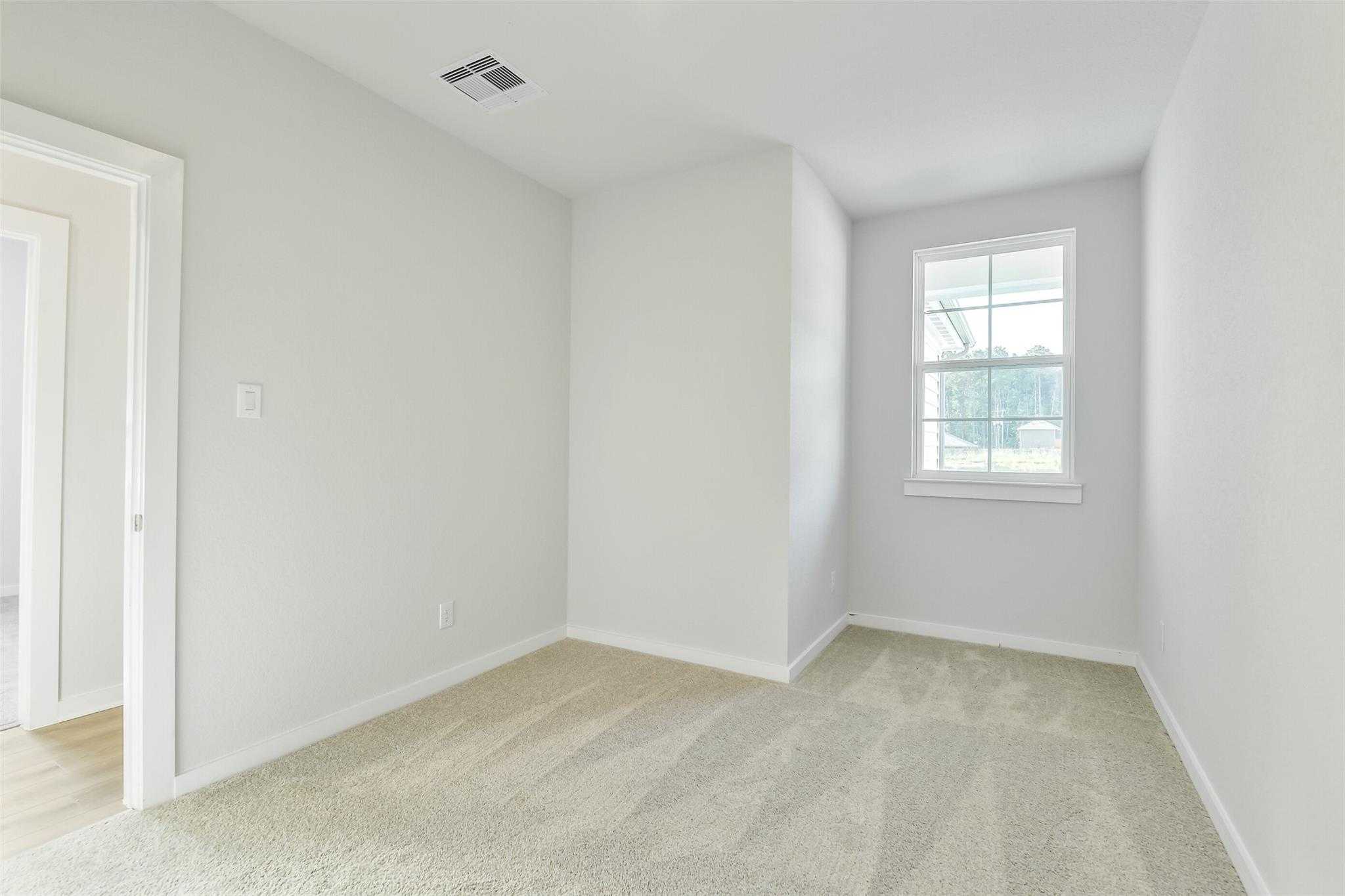 Bright empty bedroom with beige carpet, gray walls, and large window in Davidson Homes The Colorado F, Cleveland, Texas