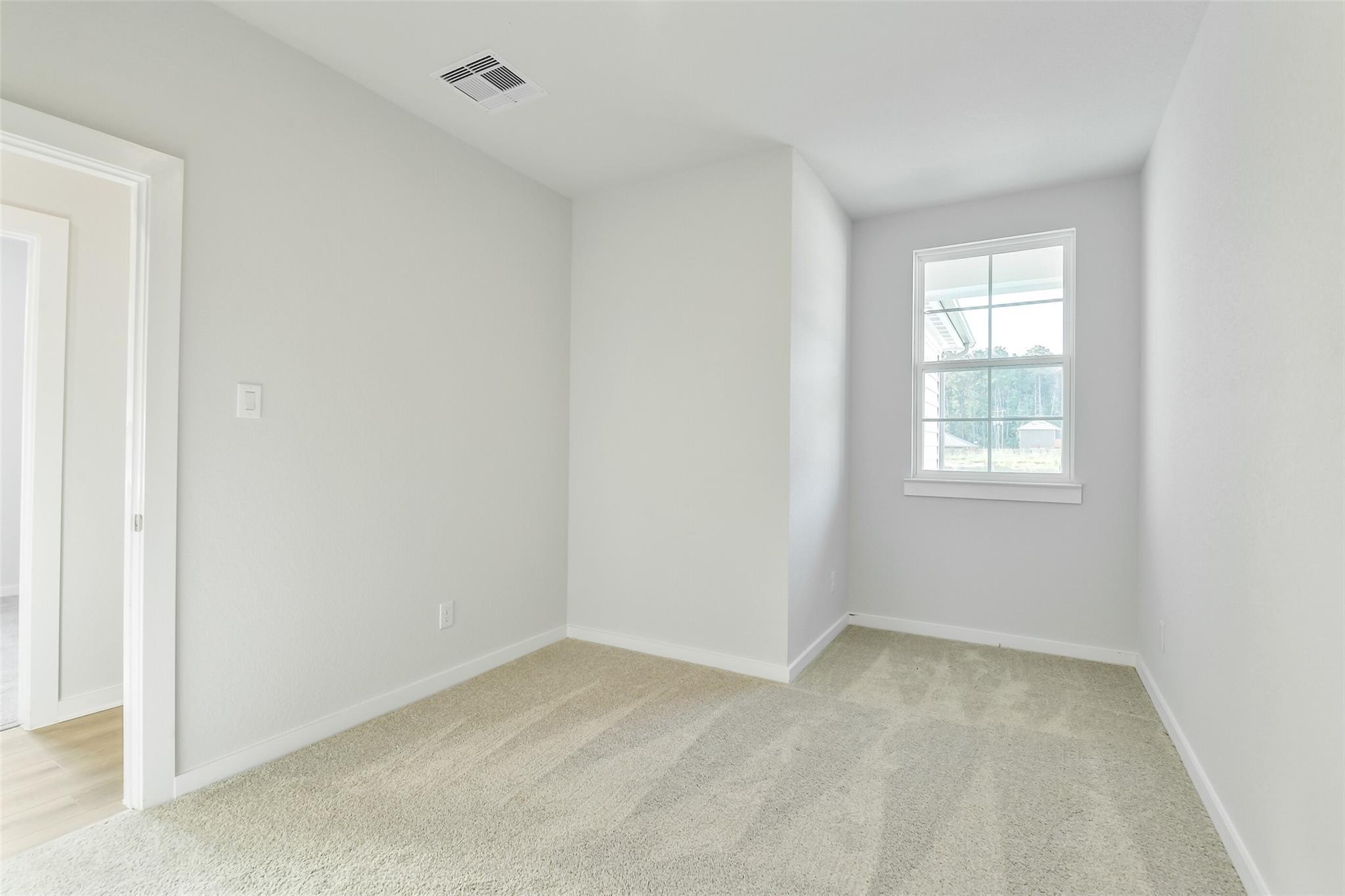Bright empty bedroom with gray walls, beige carpet, and large window in 4-bedroom Davidson Homes The Colorado F, Cleveland, Texas