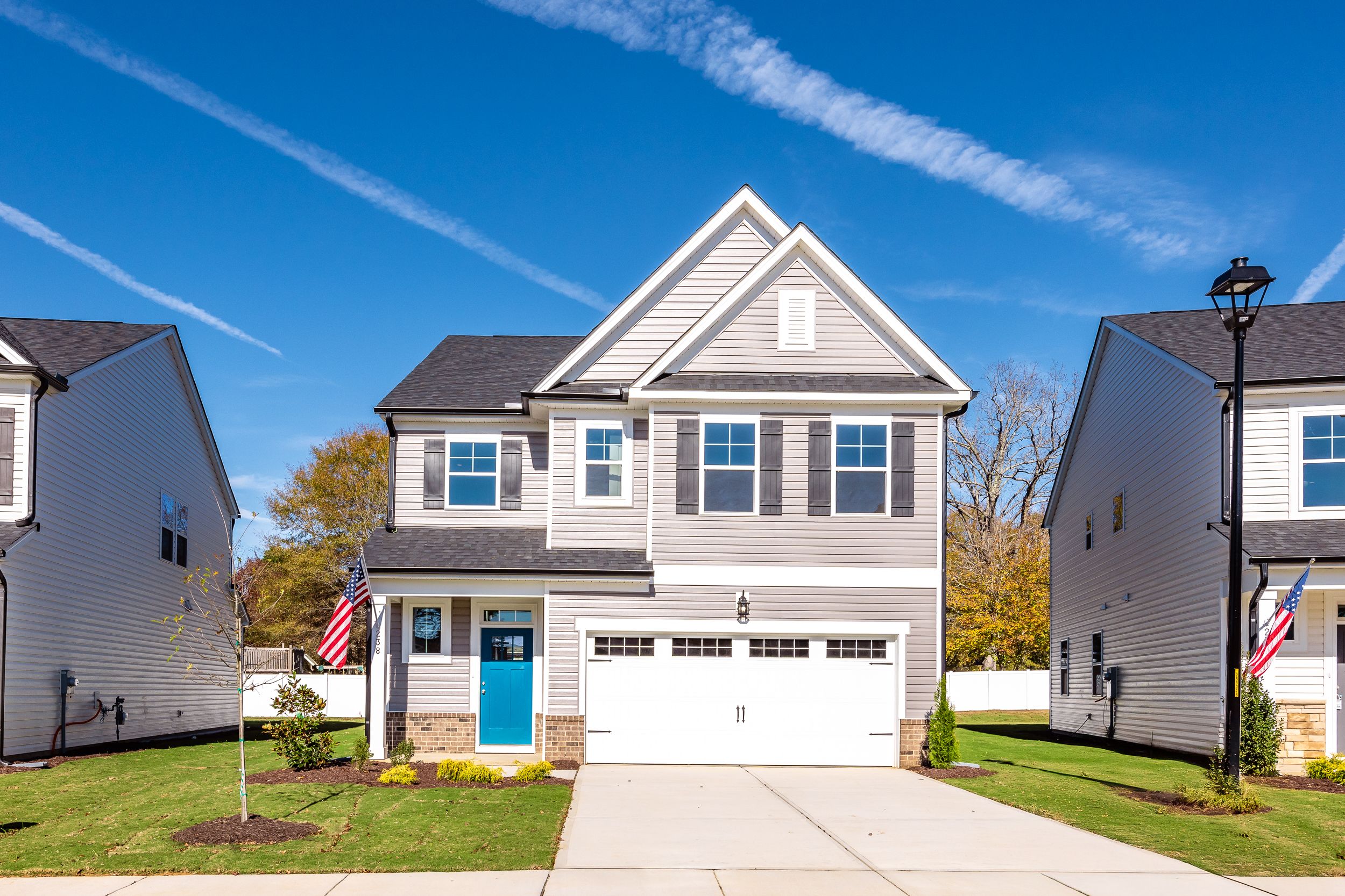Modern two-story craftsman home exterior at Gregory Village in Lillington NC with blue door, garage, flags, and landscaped yard