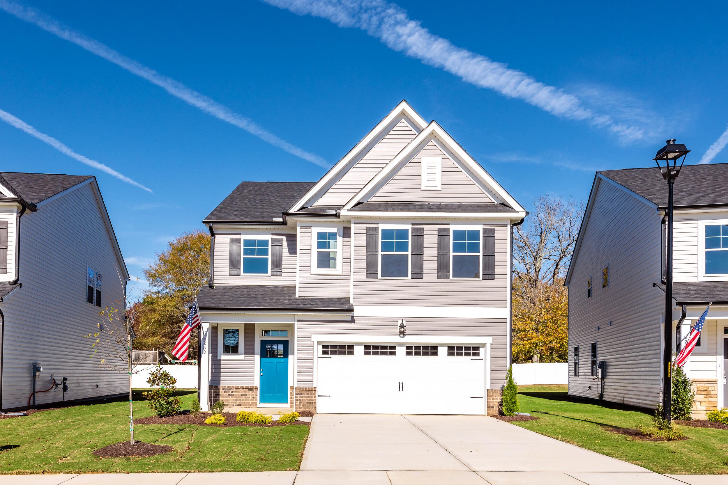 Modern two-story craftsman home exterior at Gregory Village in Lillington NC with blue door, garage, flags, and landscaped yard