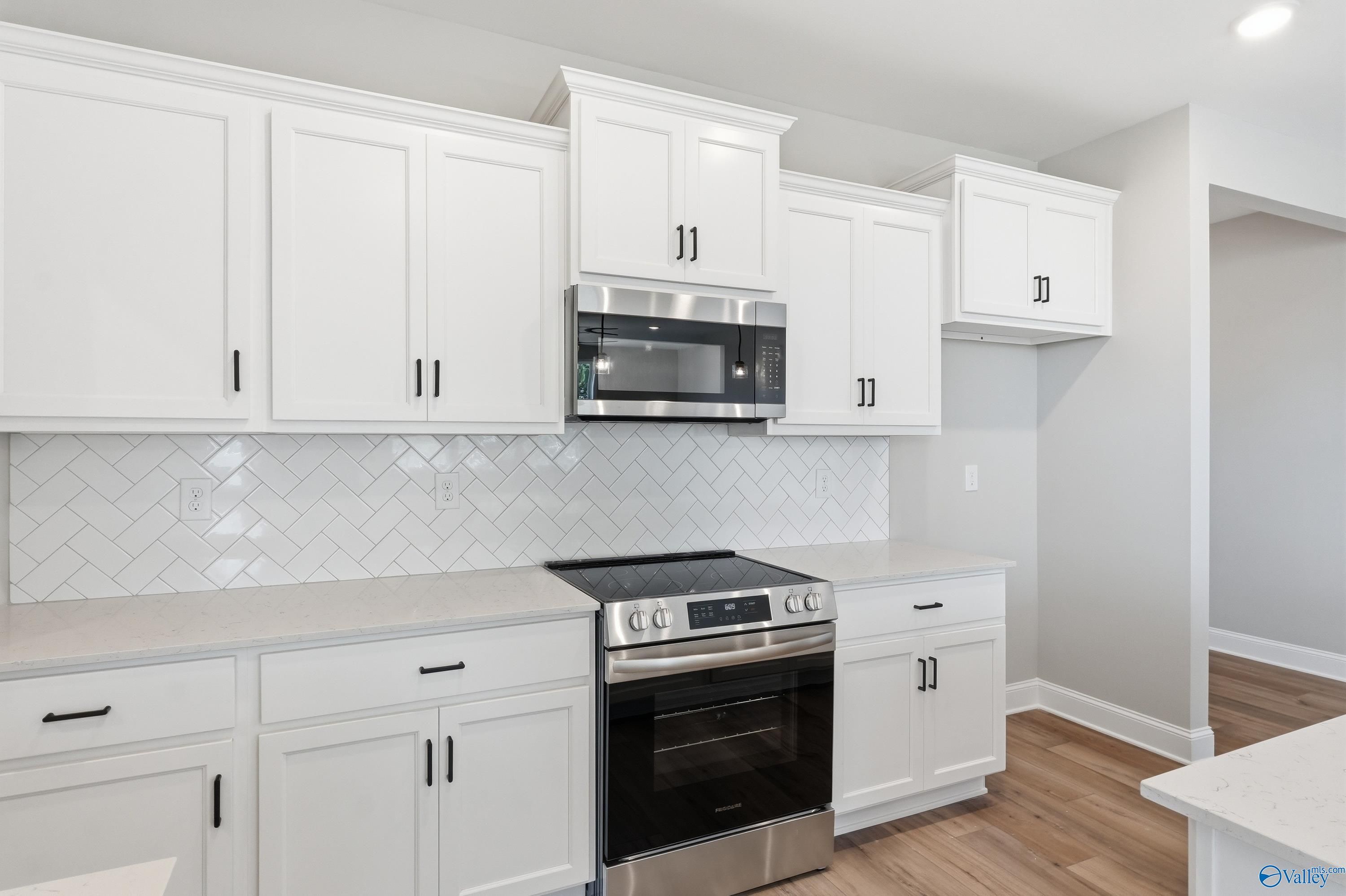 Modern white kitchen featuring stainless steel cooktop, oven, and microwave with herringbone backsplash in The Laurel K, Cullman, AL