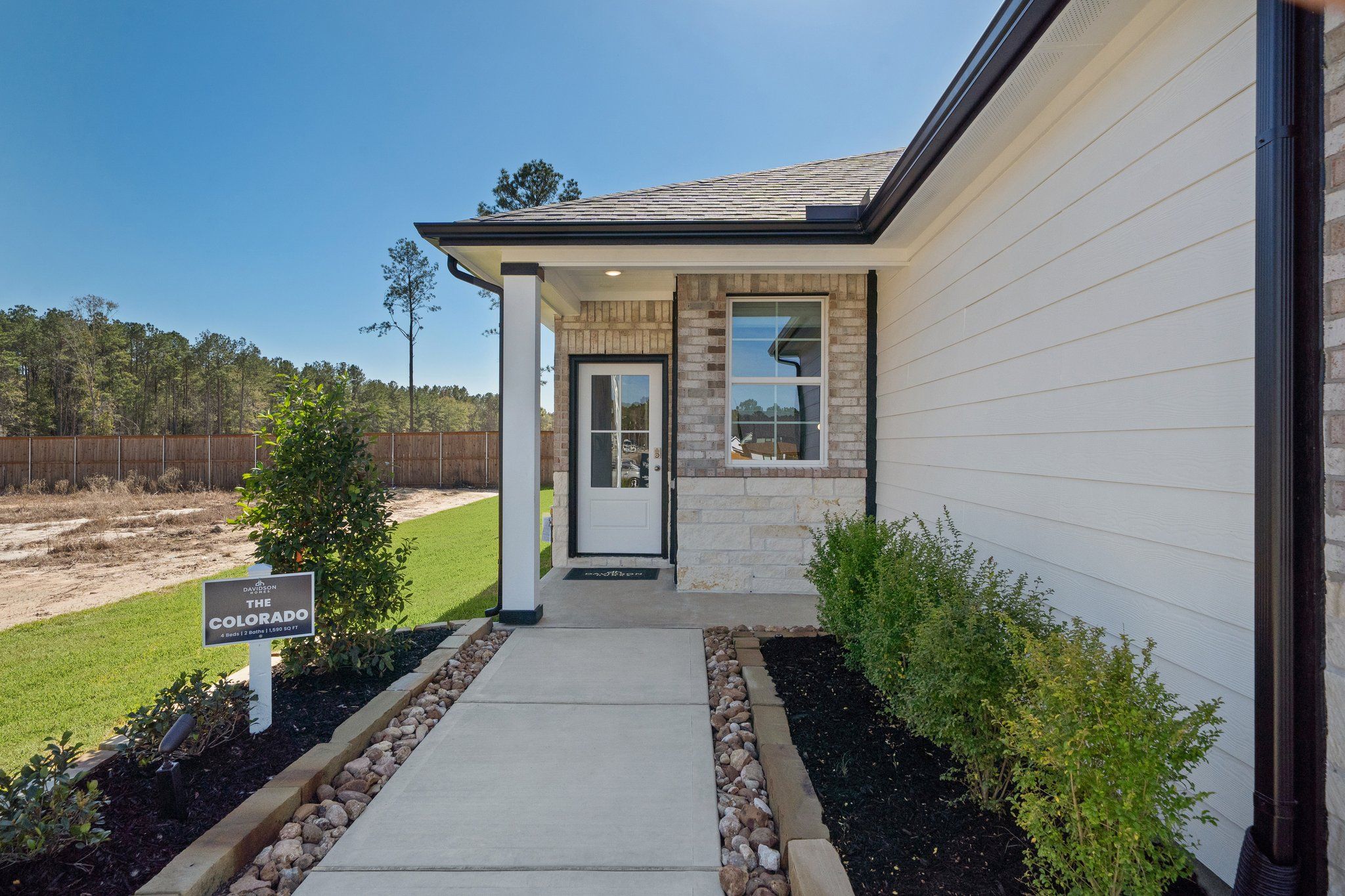Brick-accented home exterior at Spring Branch Crossing in Conroe Texas with white siding, covered entry, and landscaped path