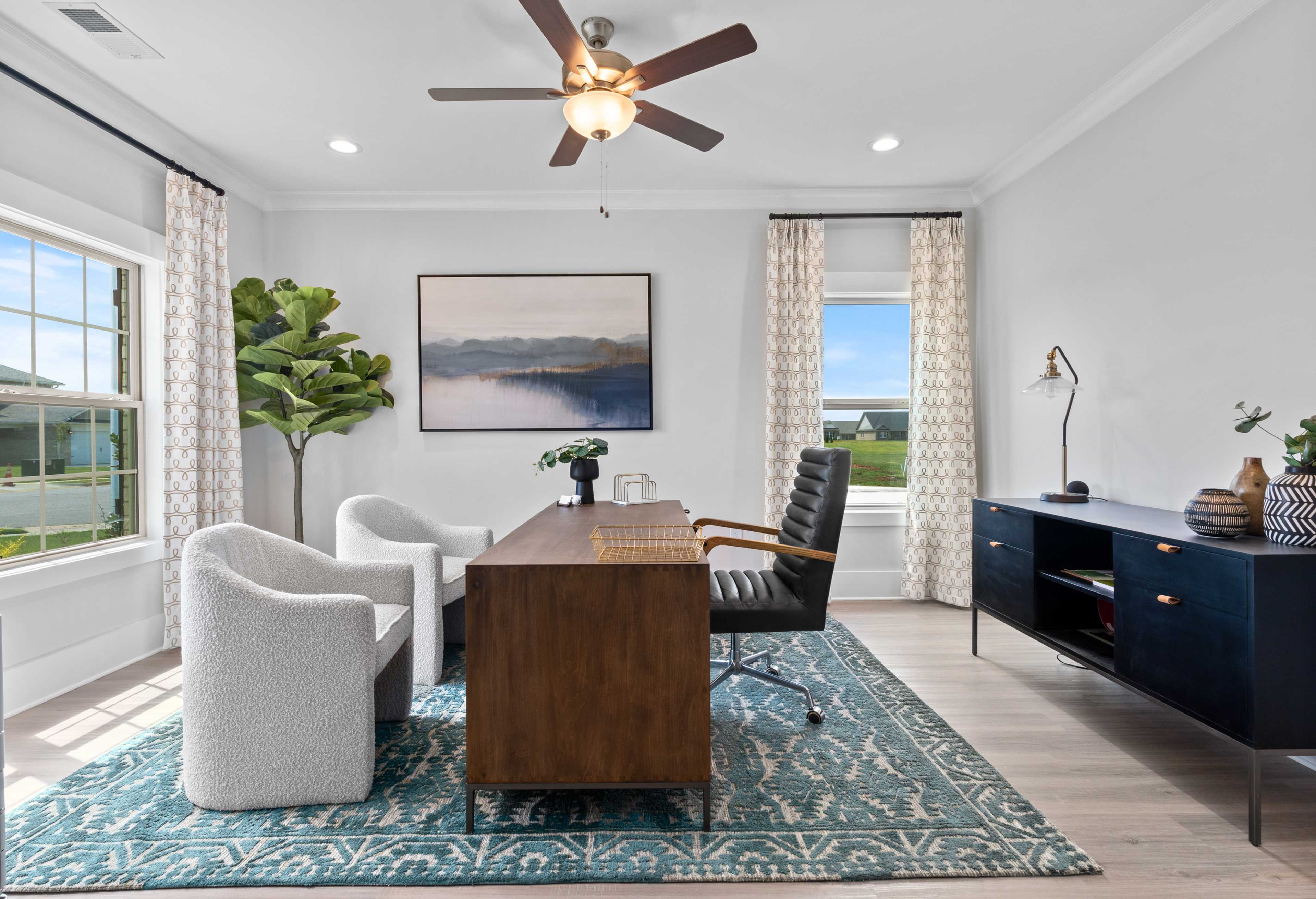 Stylish home office in The Chelsea D with wooden desk, leather chair, white armchairs, and large windows overlooking greenery