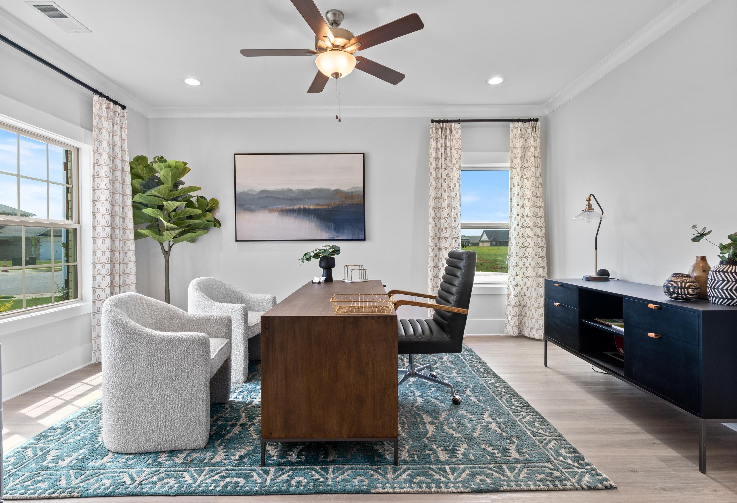 Stylish home office in The Chelsea D with wooden desk, leather chair, white armchairs, and large windows overlooking greenery