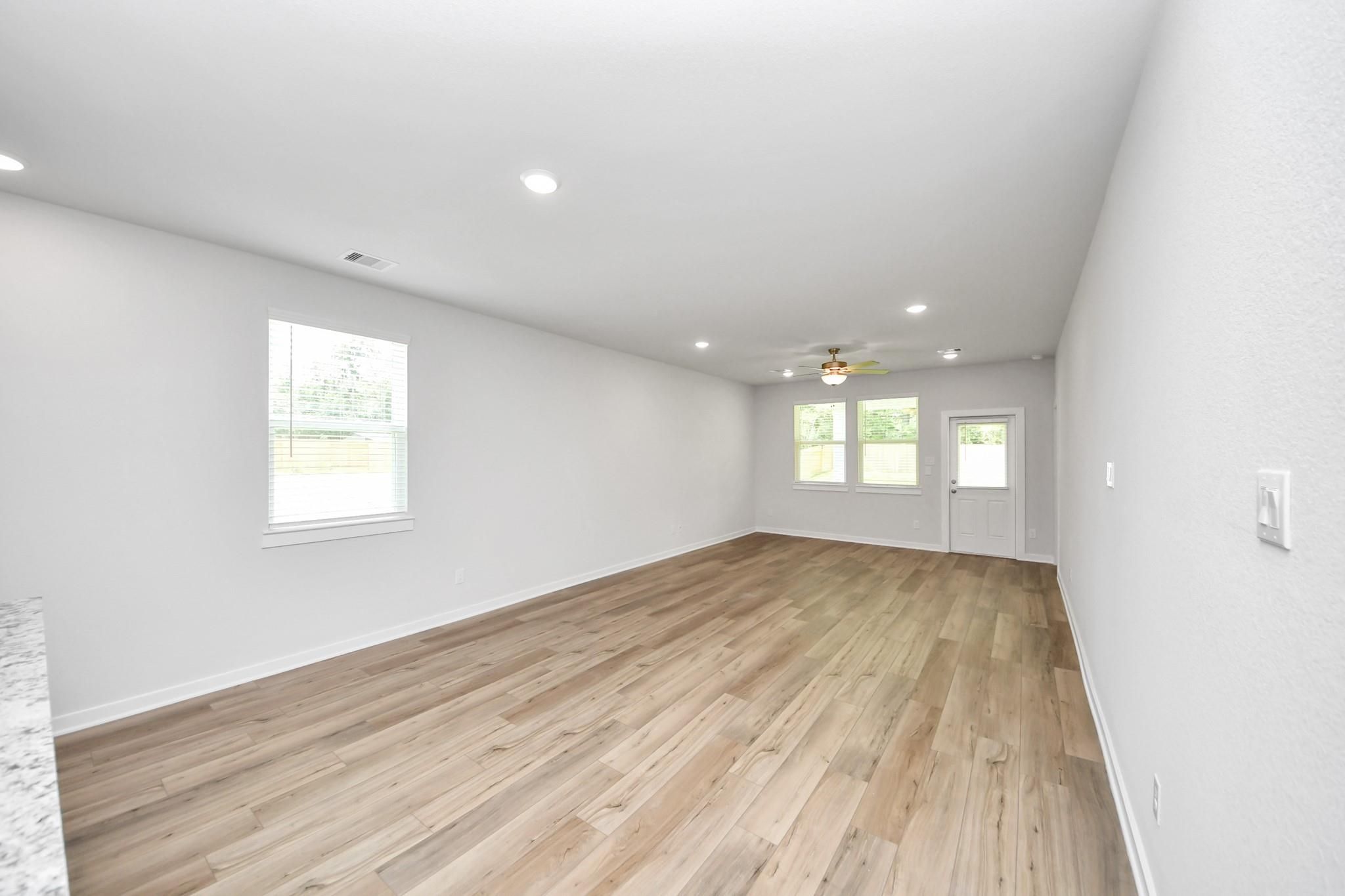 Spacious open-concept living area with wood-style flooring in The Sabine E floor plan at Liberty Estates, Cleveland, Texas.